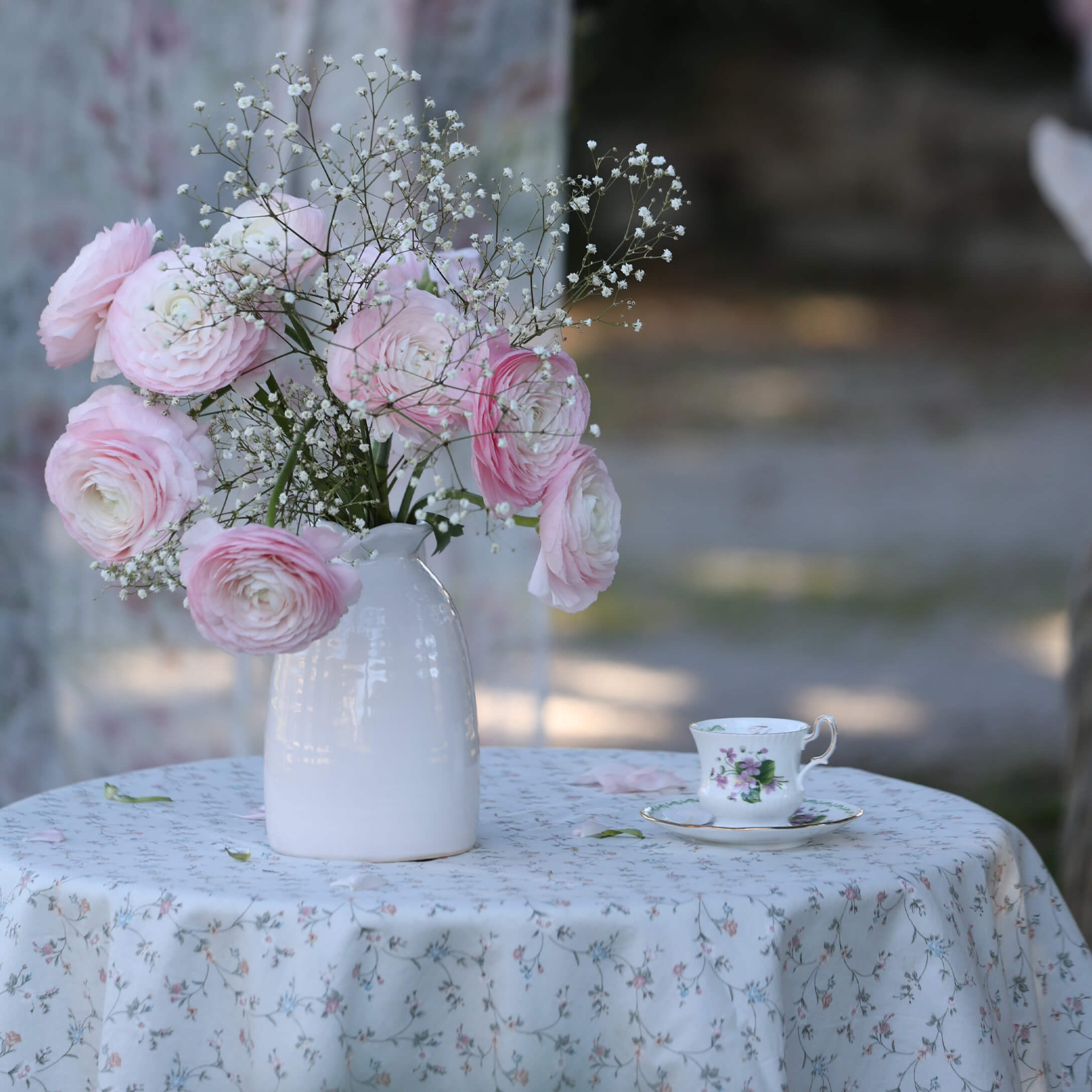 Mazetto di fiori rosa e bianchi in vaso di ceramica bianca su tavolo con tovaglia floreale