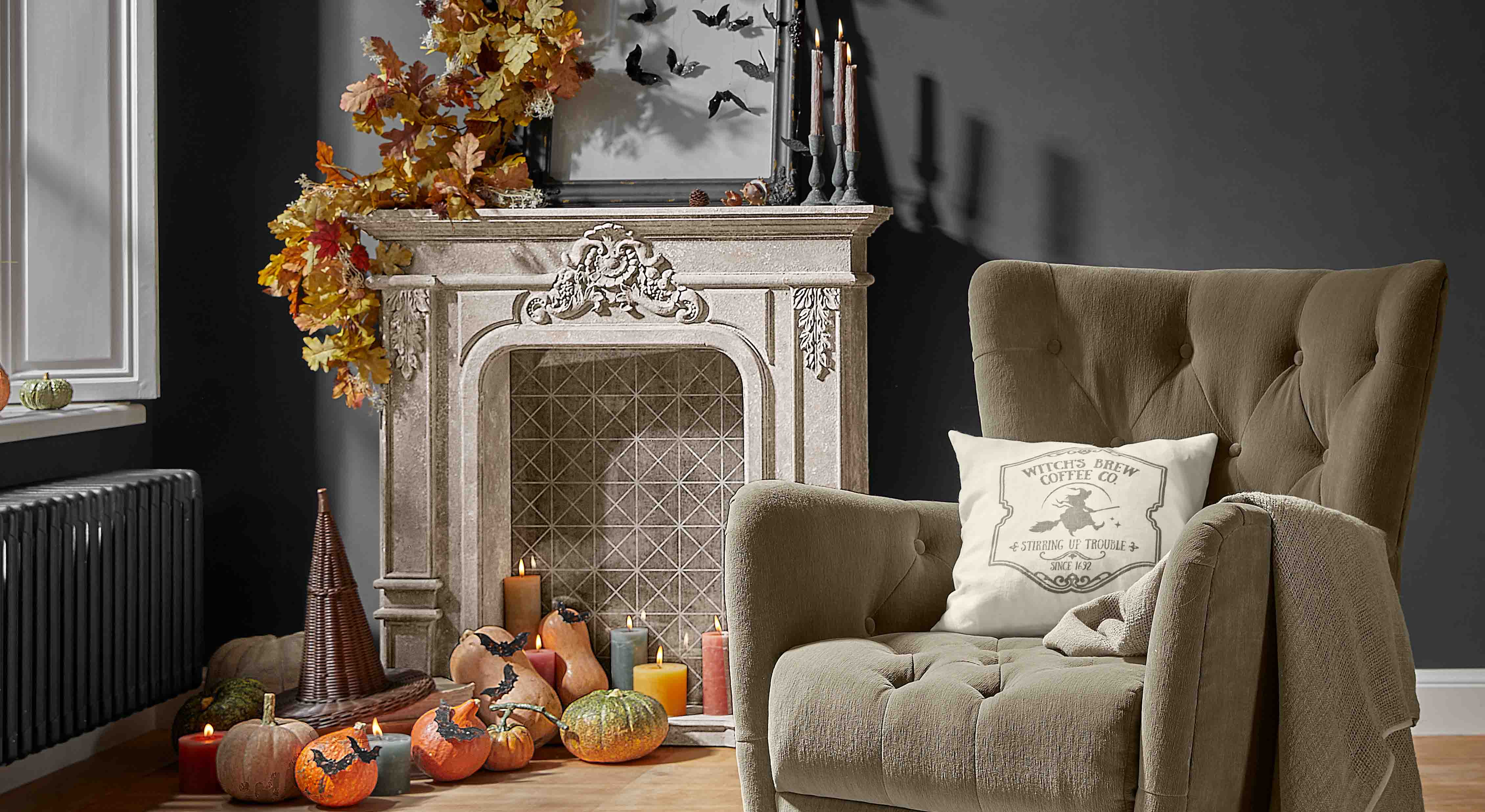 Camino decorativo con foglie autunnali, zucche e candele in soggiorno accogliente con poltrona beige