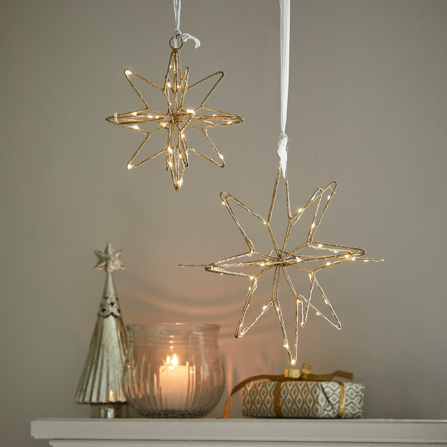 Coppia di stelle a LED Pérole Decorazioni a forma di stella dorate con luci LED sospese sopra candela e regalo su mensola bianca