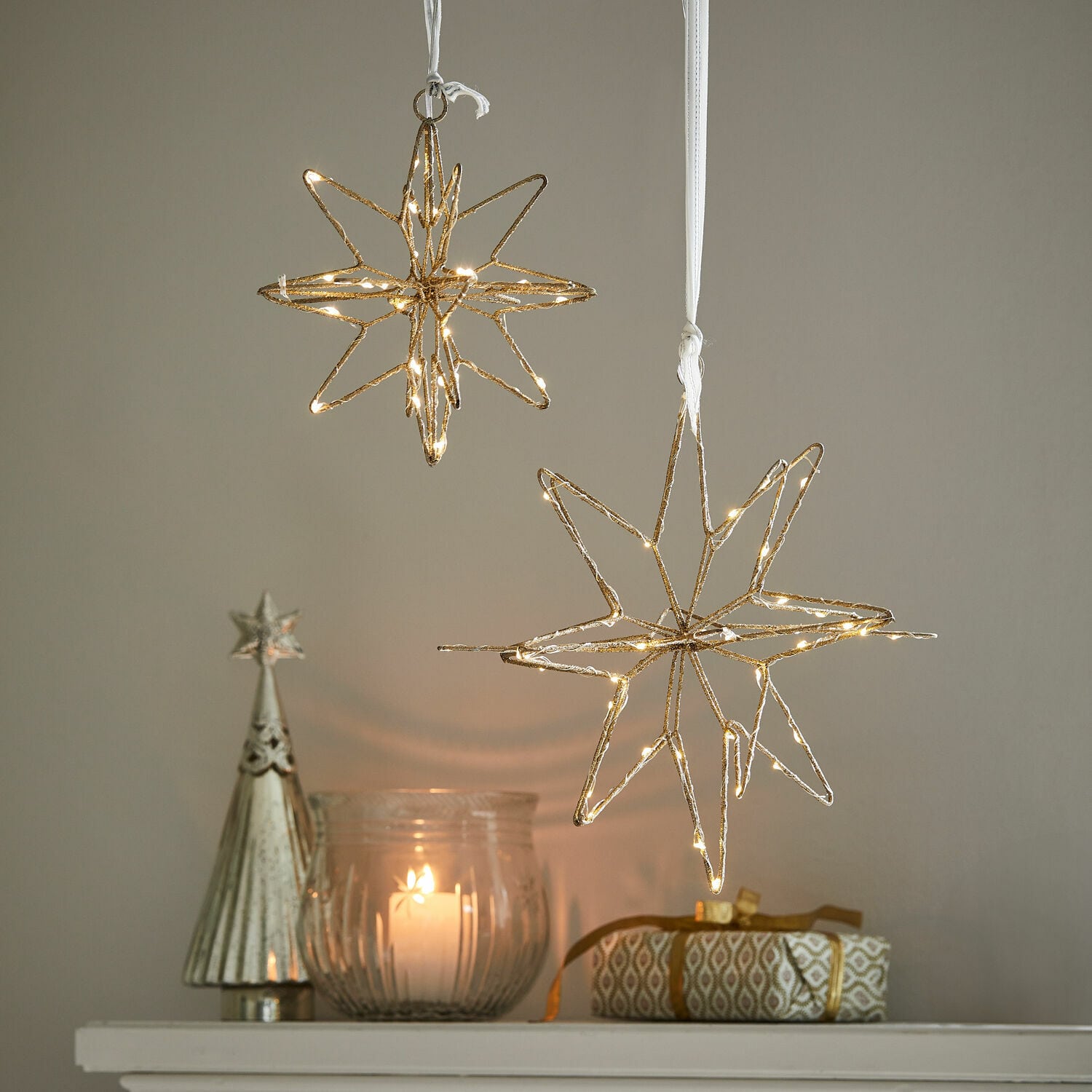 Coppia di stelle a LED Pérole Decorazioni a forma di stella dorate con luci LED sospese sopra candela e regalo su mensola bianca