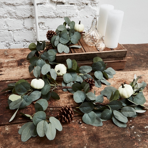 Ghirlanda decorativa con foglie verdi di eucalipto, mini zucche bianche e pigne su tavolo in legno