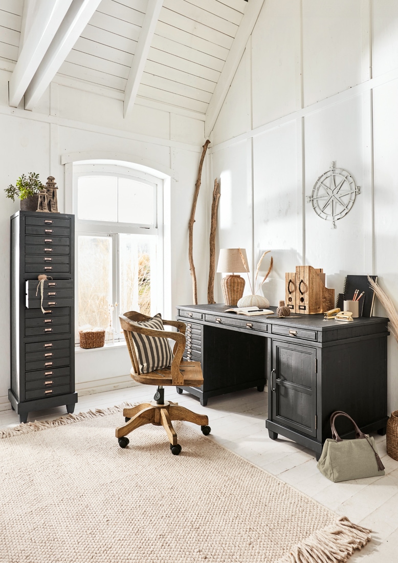 Scrivania in legno nero e armadio alto con cassetti in stanza luminosa e accogliente per lavorare