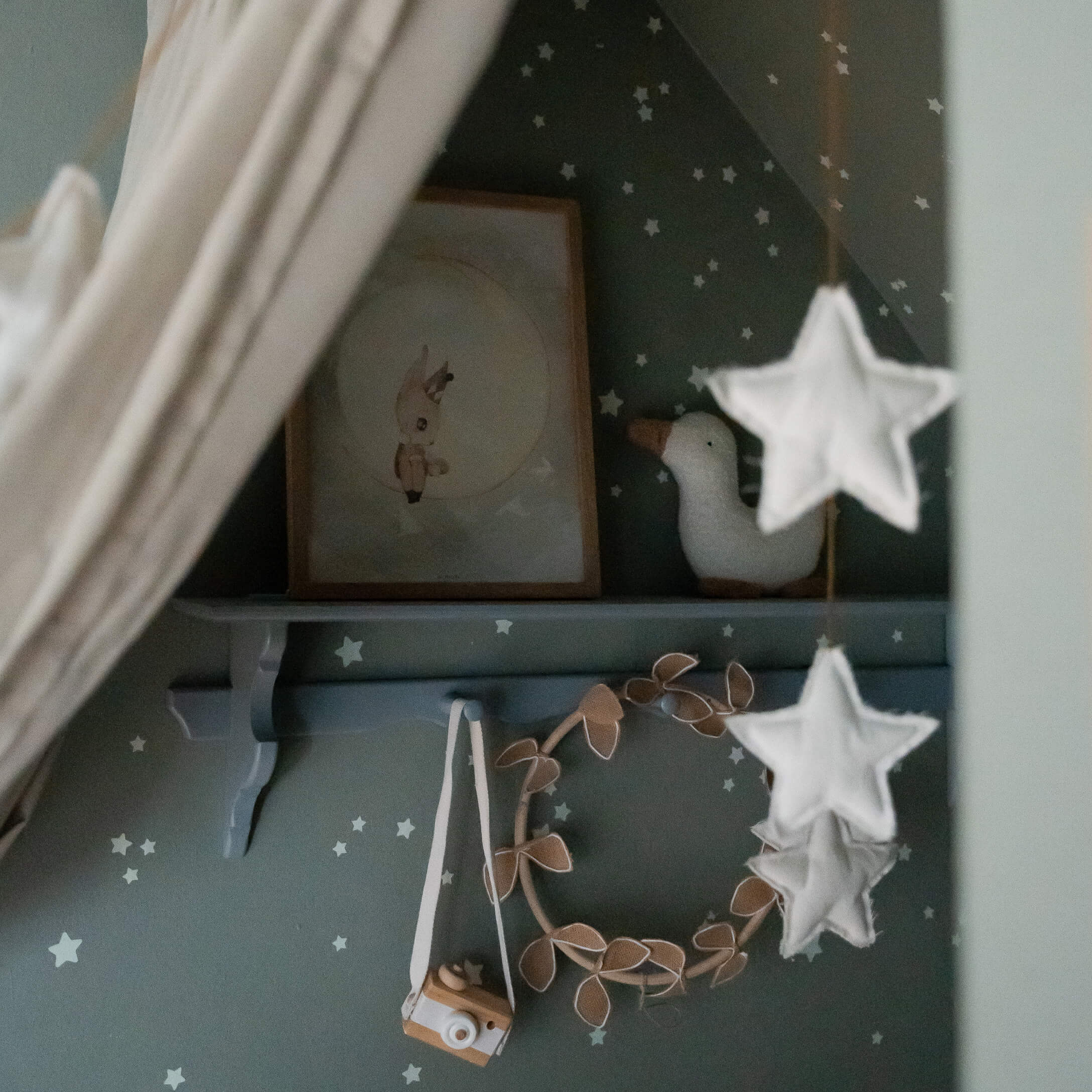 Mensola decorativa con macchina fotografica in legno, anatra di peluche e quadro in stanza per bambini con stelle.