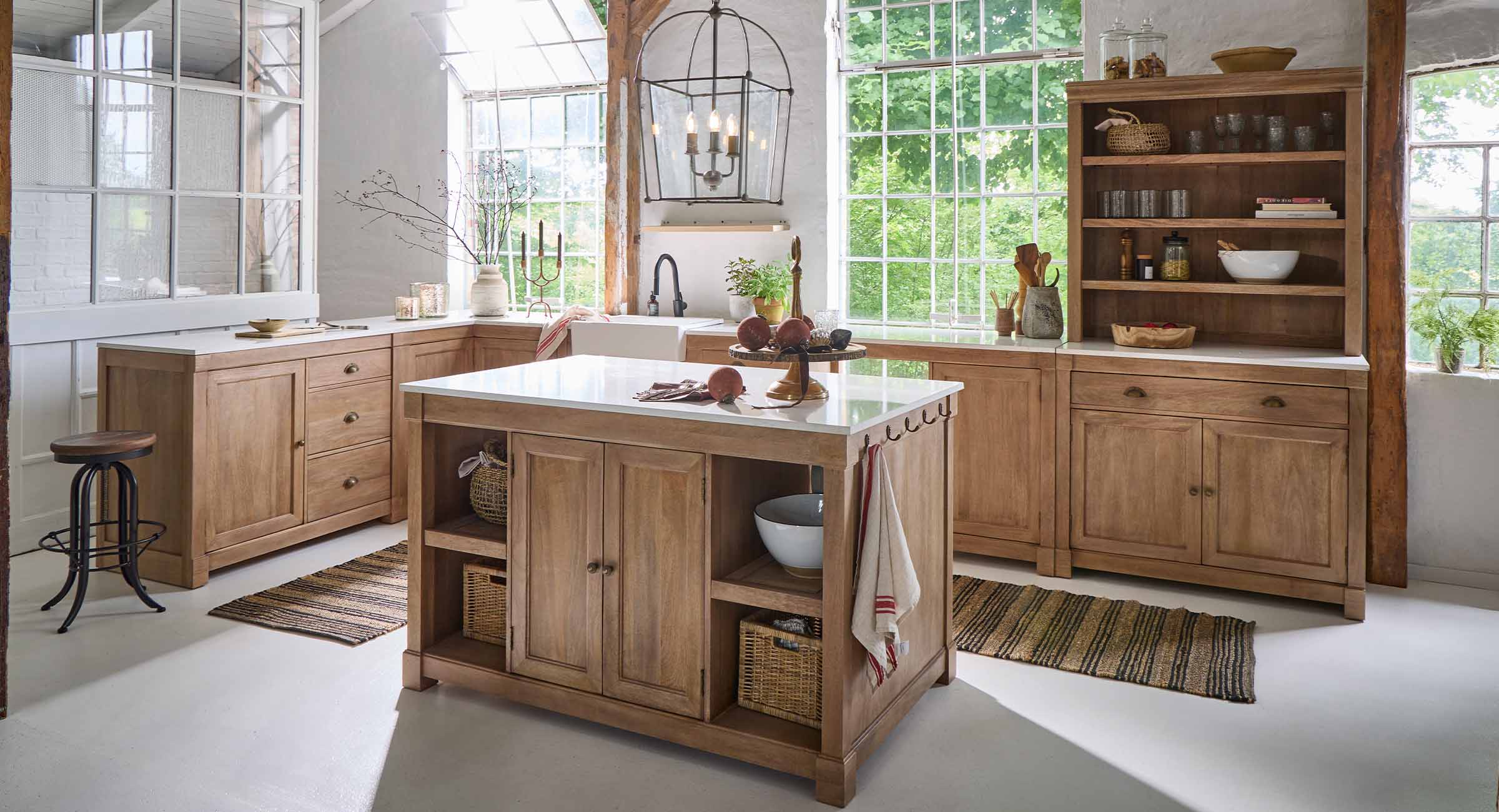 Cucina con isola e mobili in rovere naturale, piani bianchi e grandi finestre luminose