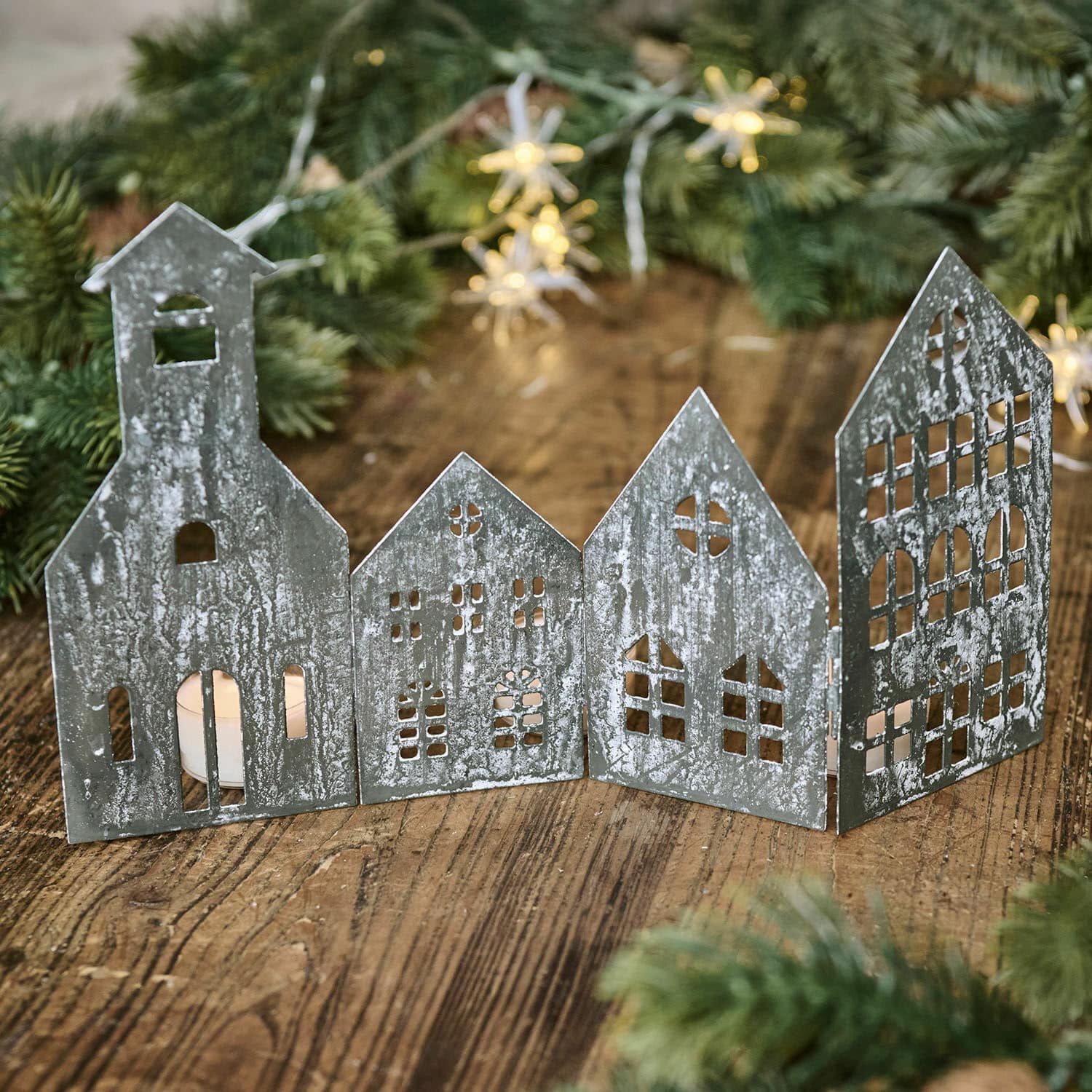 Divisorio decorativo Ulorin Decorazione in metallo a forma di casette con finestre ritagliate e candela accesa su tavolo di legno con rami verdi