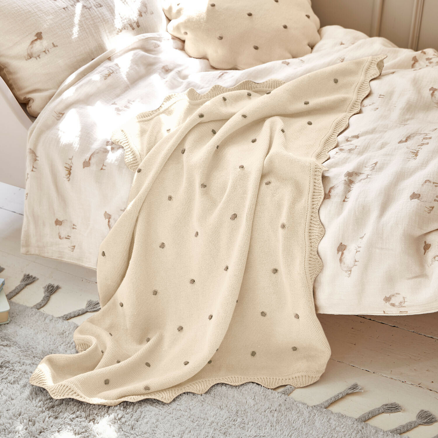 Plaid Saphie Coperta beige lavorata a maglia con pois grigi su letto con biancheria chiara e cuscino naturale