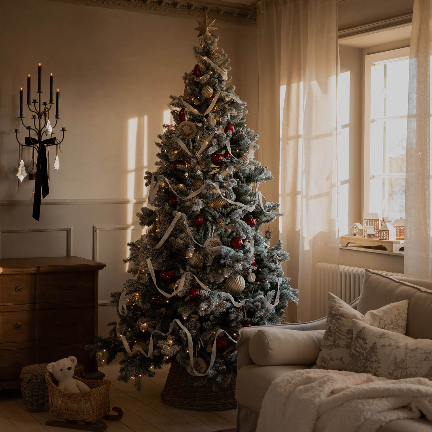 Soggiorno accogliente con albero di Natale innevato decorato con palline rosse, dorate e nastro bianco