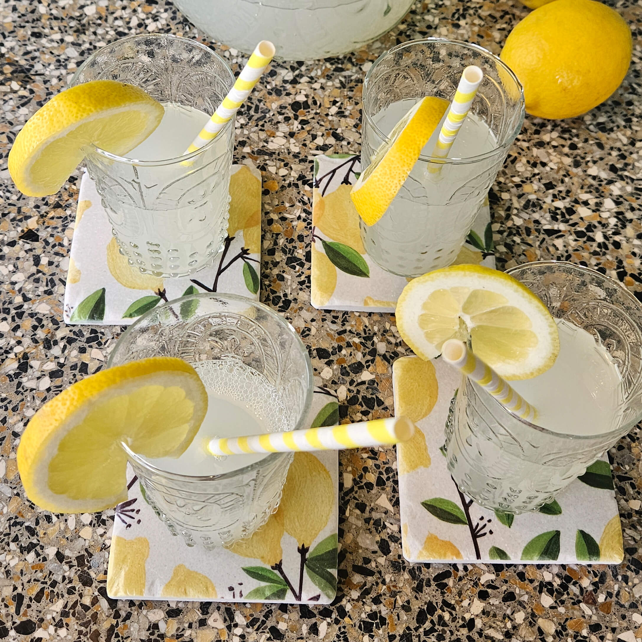 Bicchieri di limonata con fette di limone su sottobicchieri in ceramica con motivo limone su piano in pietra