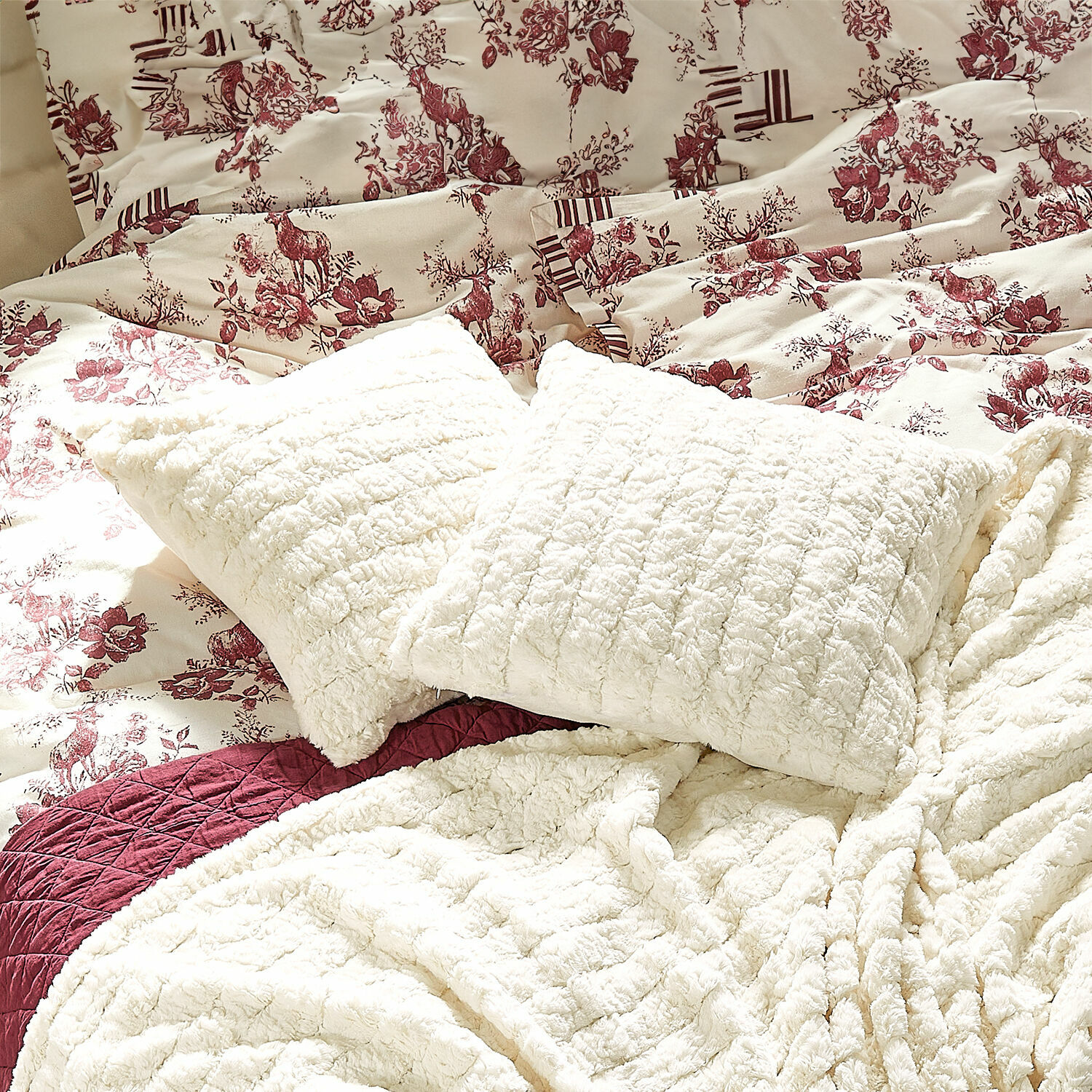 Copricuscino Dorelice Cuscini e coperte in peluche crema su letto con biancheria da letto a motivi floreali e cervi bordeaux