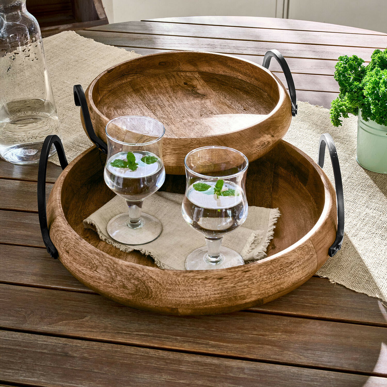 Vassoi rotondi in legno con manici in metallo su tavolo con due bicchieri d'acqua alla menta