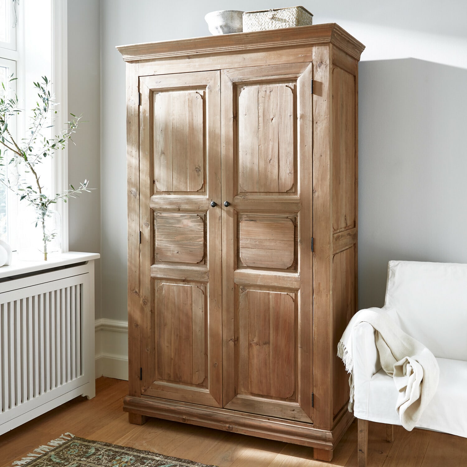Armadio Gavrielle Armadio in legno colore naturale in stanza luminosa con poltrona bianca e tappeto decorativo