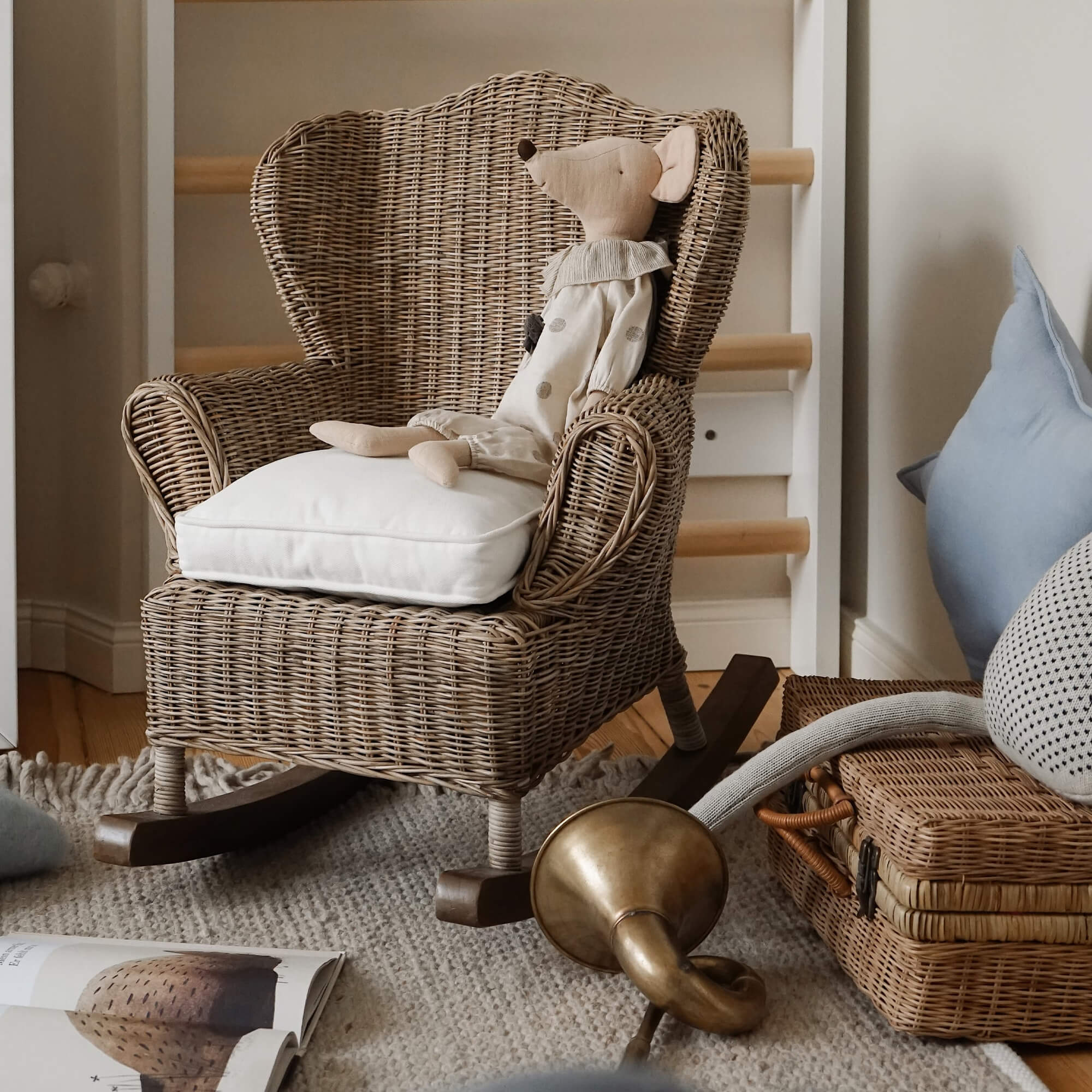 Sedia a dondolo in rattan naturale con cuscino bianco e topo di peluche in camera dei bambini