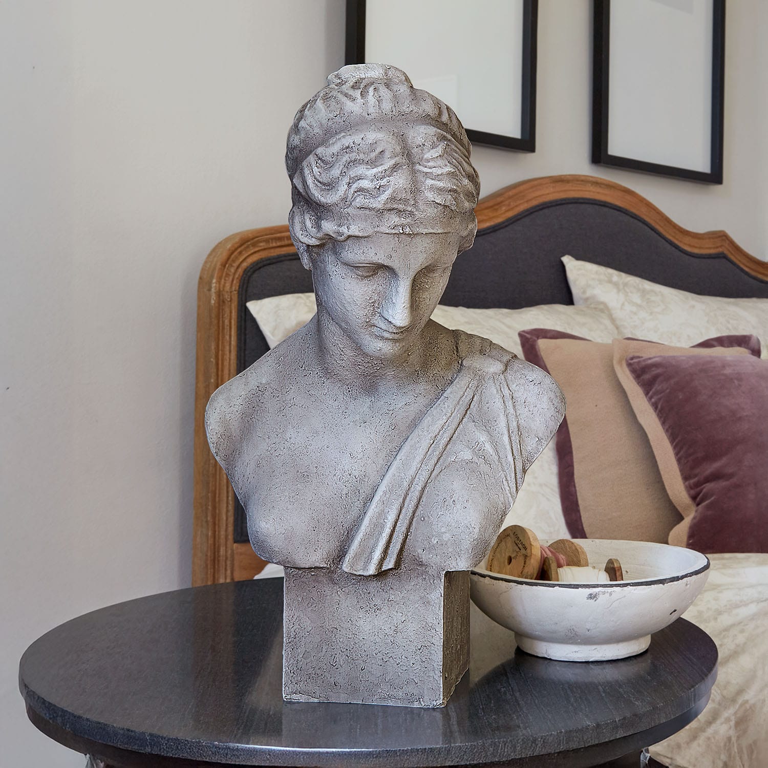 Busto in pietra grigia su tavolo nero in camera elegante con cuscini decorativi