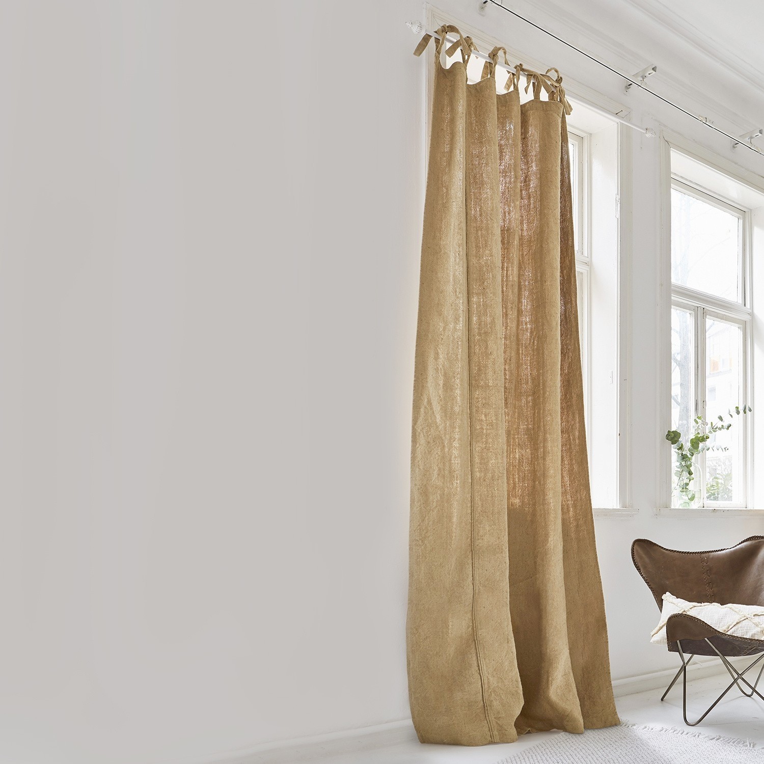 Tenda Uma Tenda beige in lino naturale in stanza luminosa con grande finestra e poltrona marrone