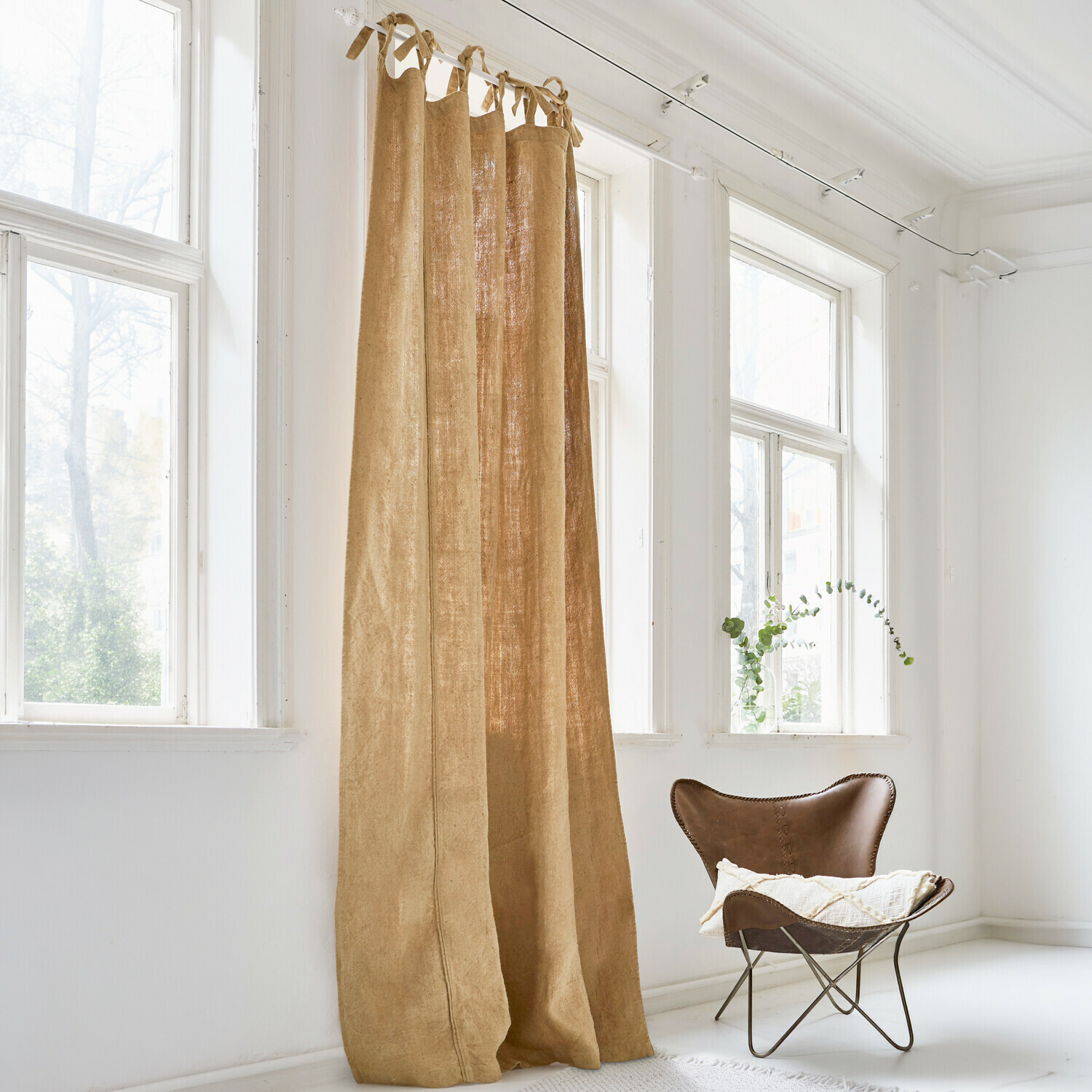 Tenda Uma Tenda beige in lino naturale in stanza luminosa con grande finestra e poltrona marrone