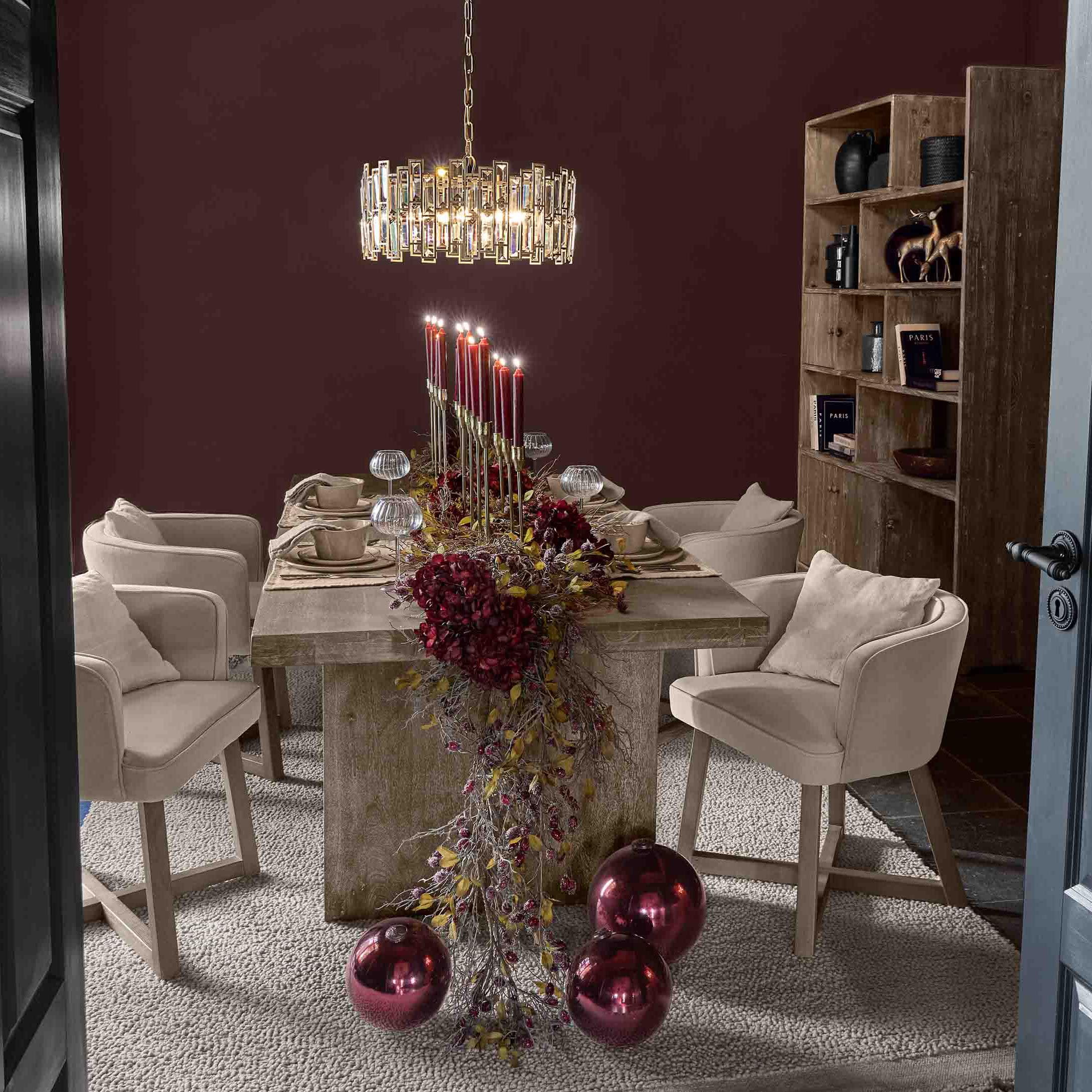 Sala da pranzo con tavolo in legno, sedie beige e decorazioni con candele rosse e palline natalizie lucide