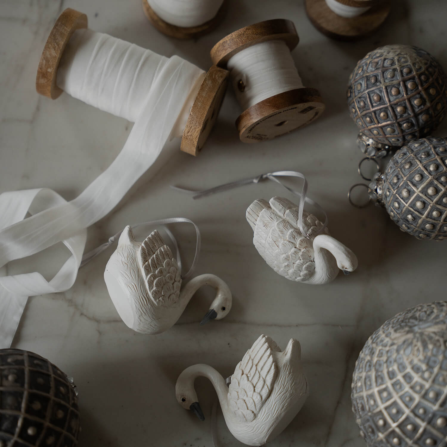 Decorazioni cigni in ceramica bianca con nastro e rocchetti di legno con nastro bianco su tavolo in marmo