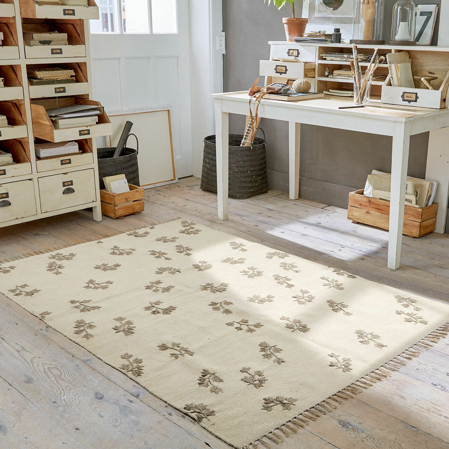 Tappeto Galorique Tappeto beige con motivo floreale e frange su pavimento in legno in stanza luminosa da lavoro