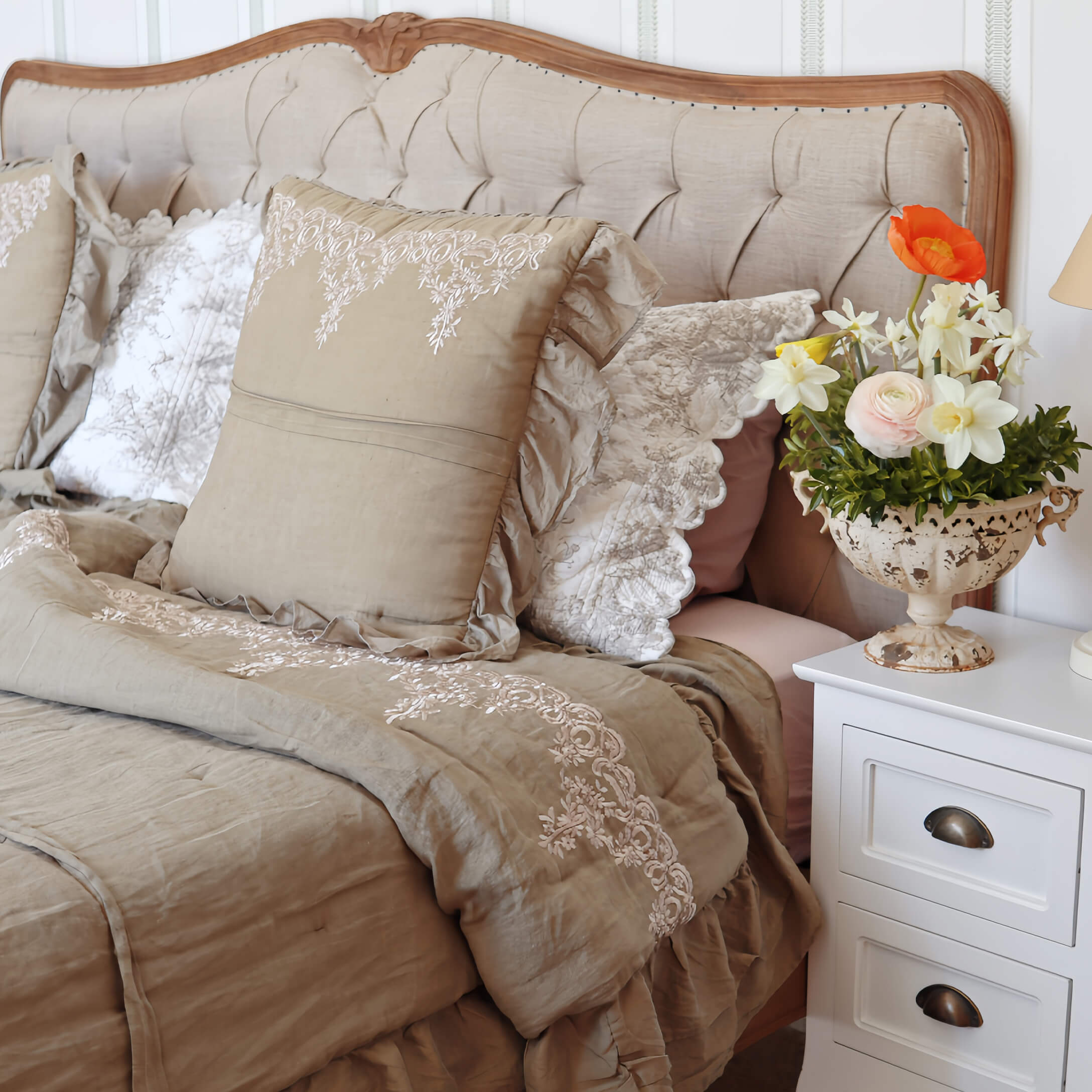Biancheria da letto beige con cuscini ricamati e coperta su letto con testiera imbottita