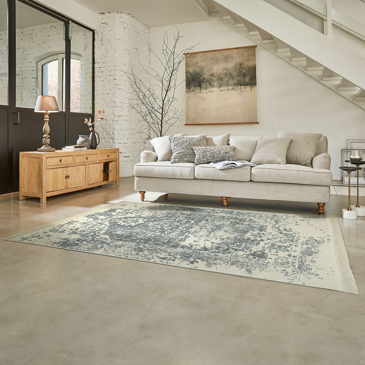 Tappeto Lortet Divano beige con cuscini su tappeto grigio in soggiorno luminoso con mobile in legno e decorazione a parete