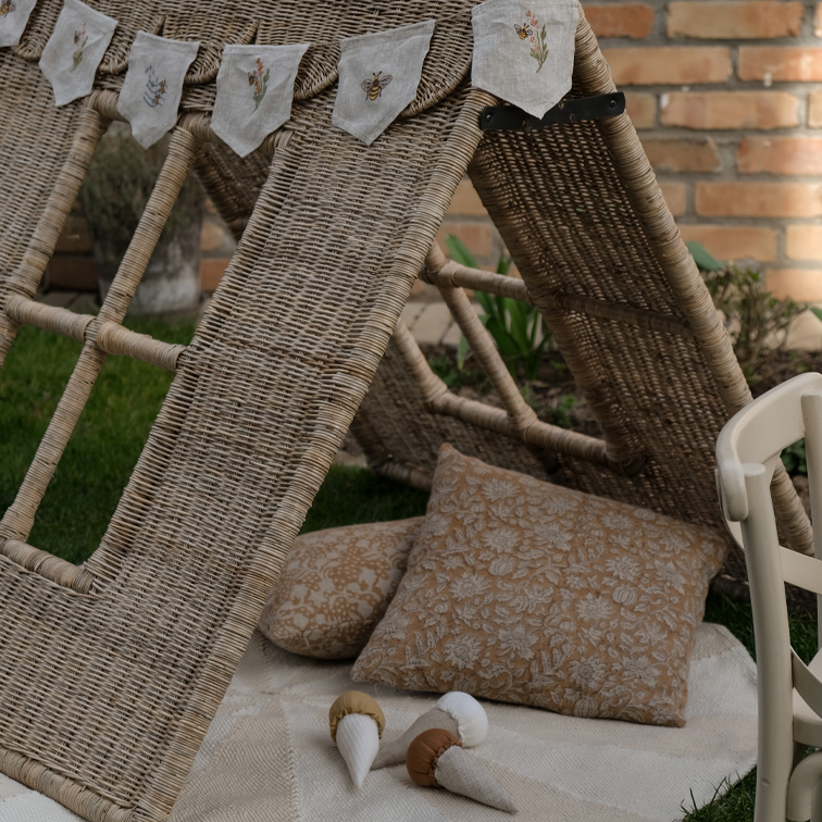 Tenda in vimini con cuscini e ghirlanda di lino ricamata in giardino, materiali naturali e atmosfera accogliente