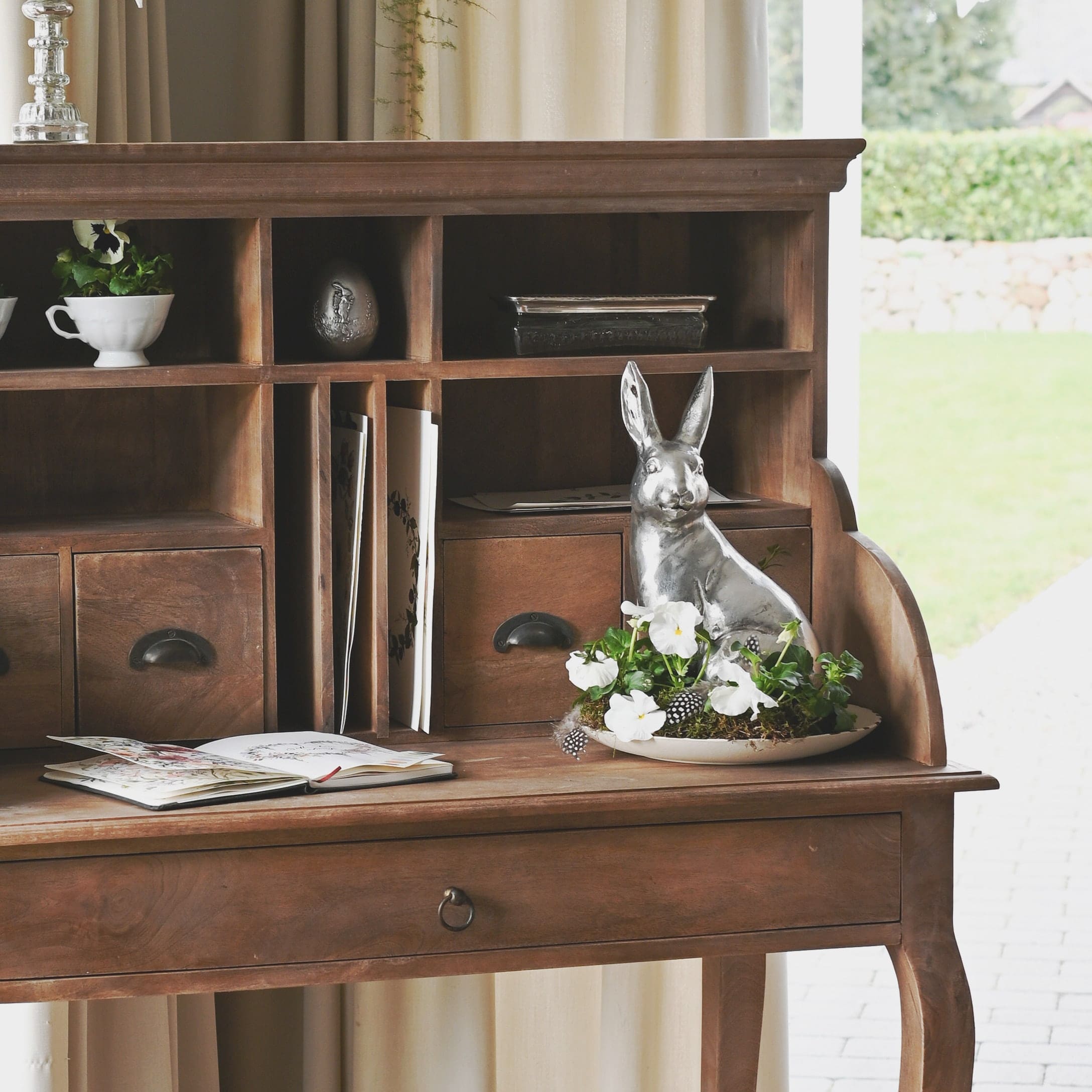 Scrivania in legno con cassetti e decorazione con coniglio argentato e fiori bianchi su piatto