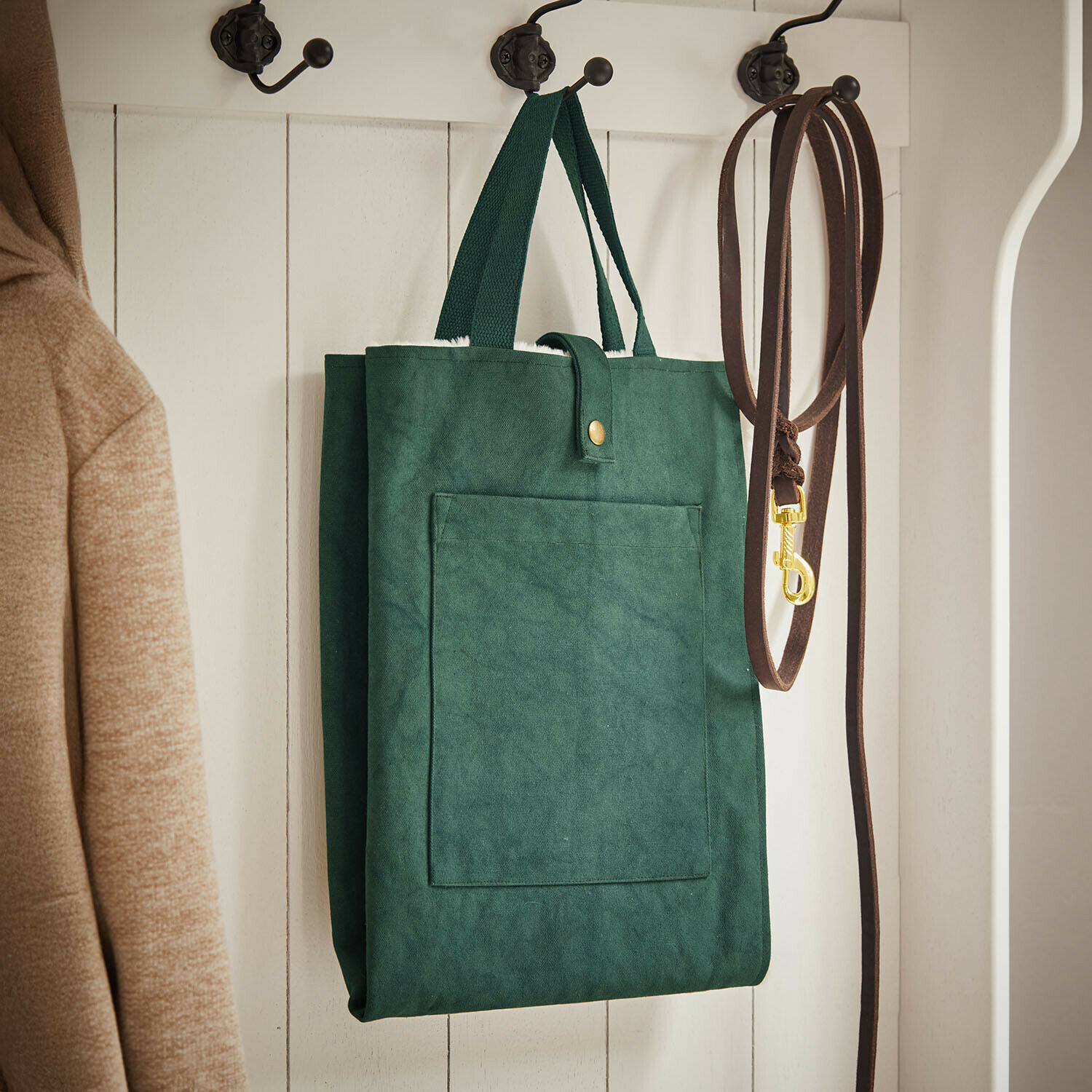 Tappetino per animali Felliro Borsa verde in tessuto appesa a appendiabiti bianco accanto a guinzaglio marrone e cappotto beige