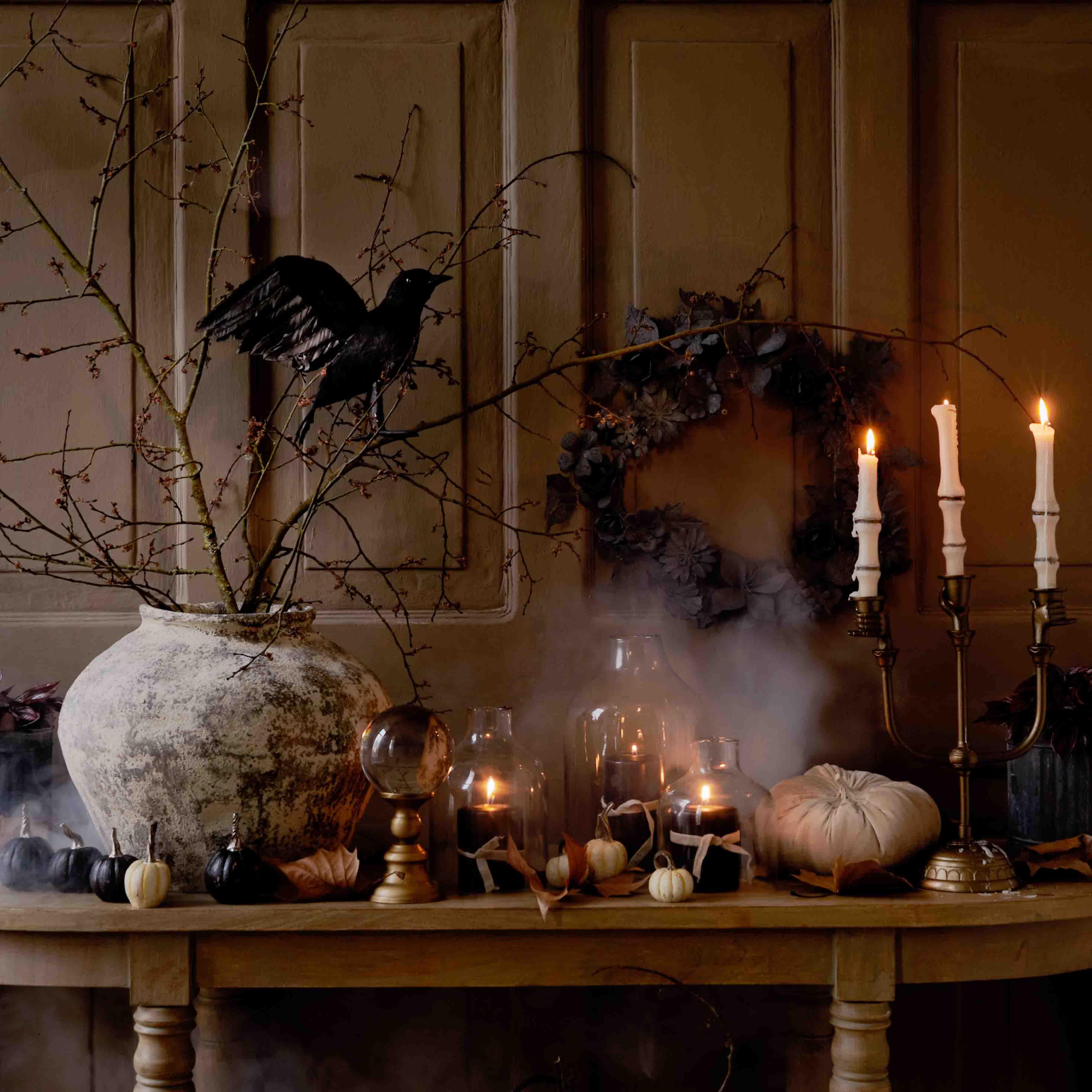 Decorazione autunnale da tavolo con grande vaso in ceramica, candele accese e uccello nero su ramo