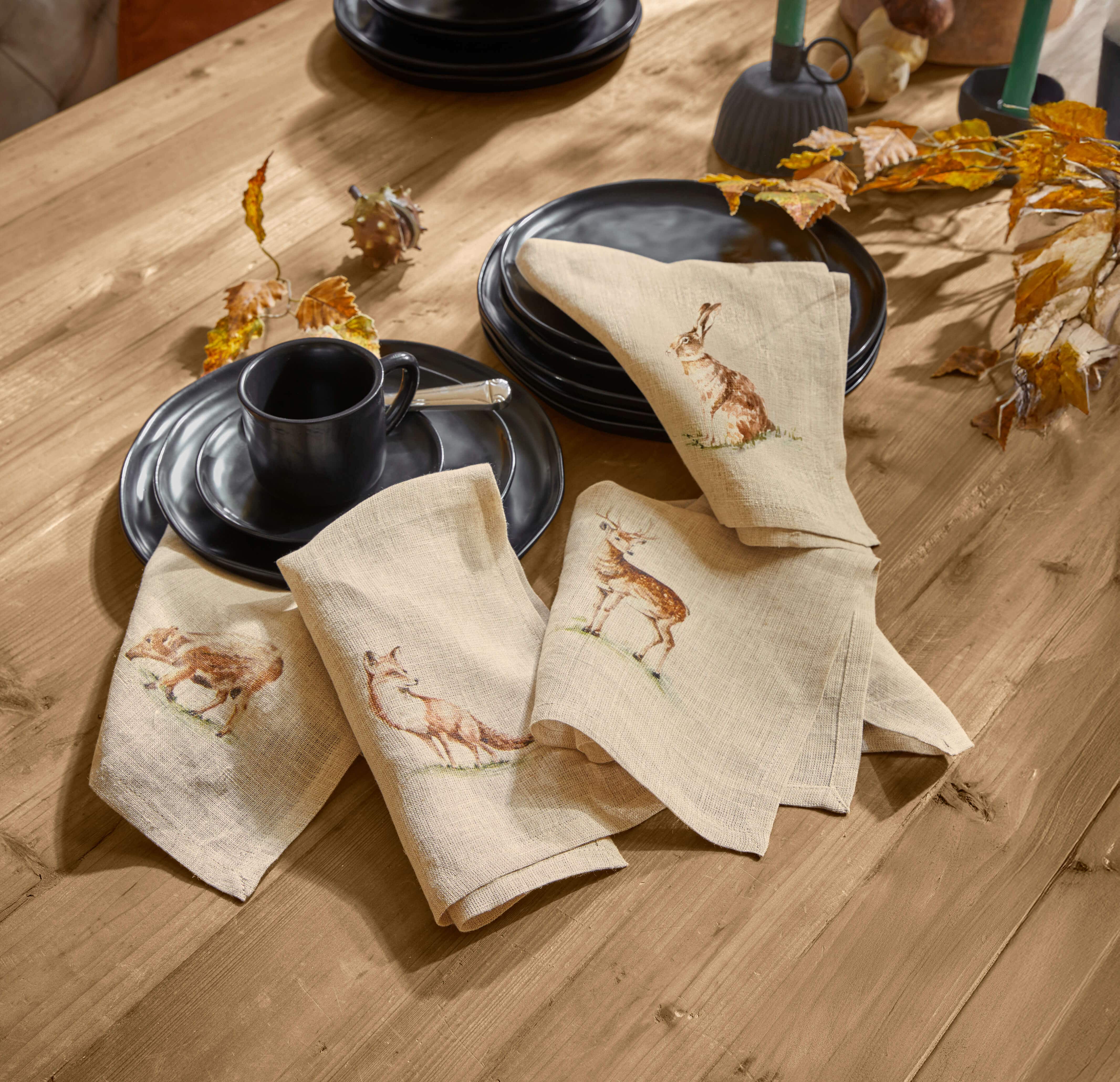 Tovaglioli in lino beige con stampe di animali della foresta su tavolo in legno con stoviglie nere