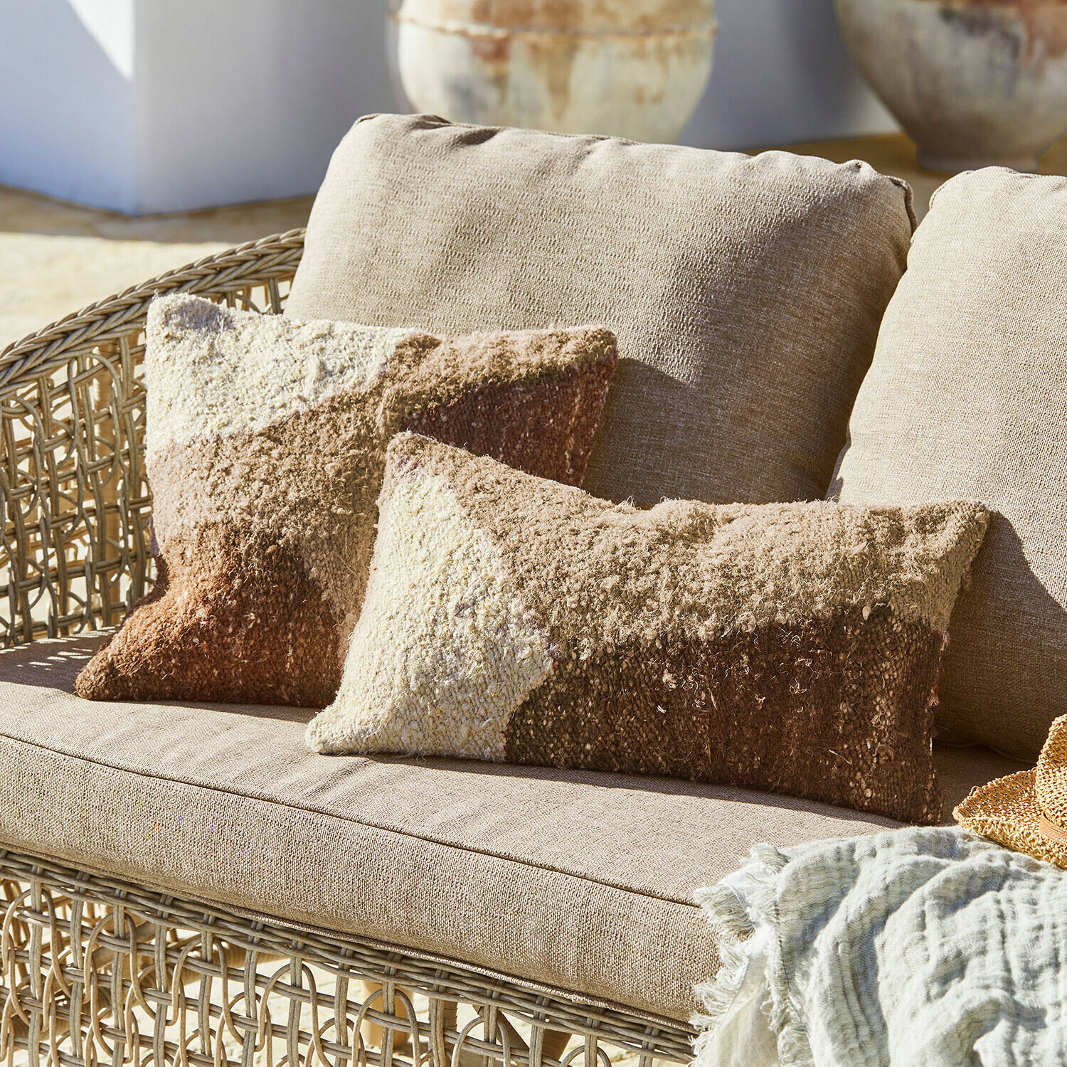 Divano in rattan beige con cuscini morbidi in tonalità marrone e crema, coperta tessile decorativa