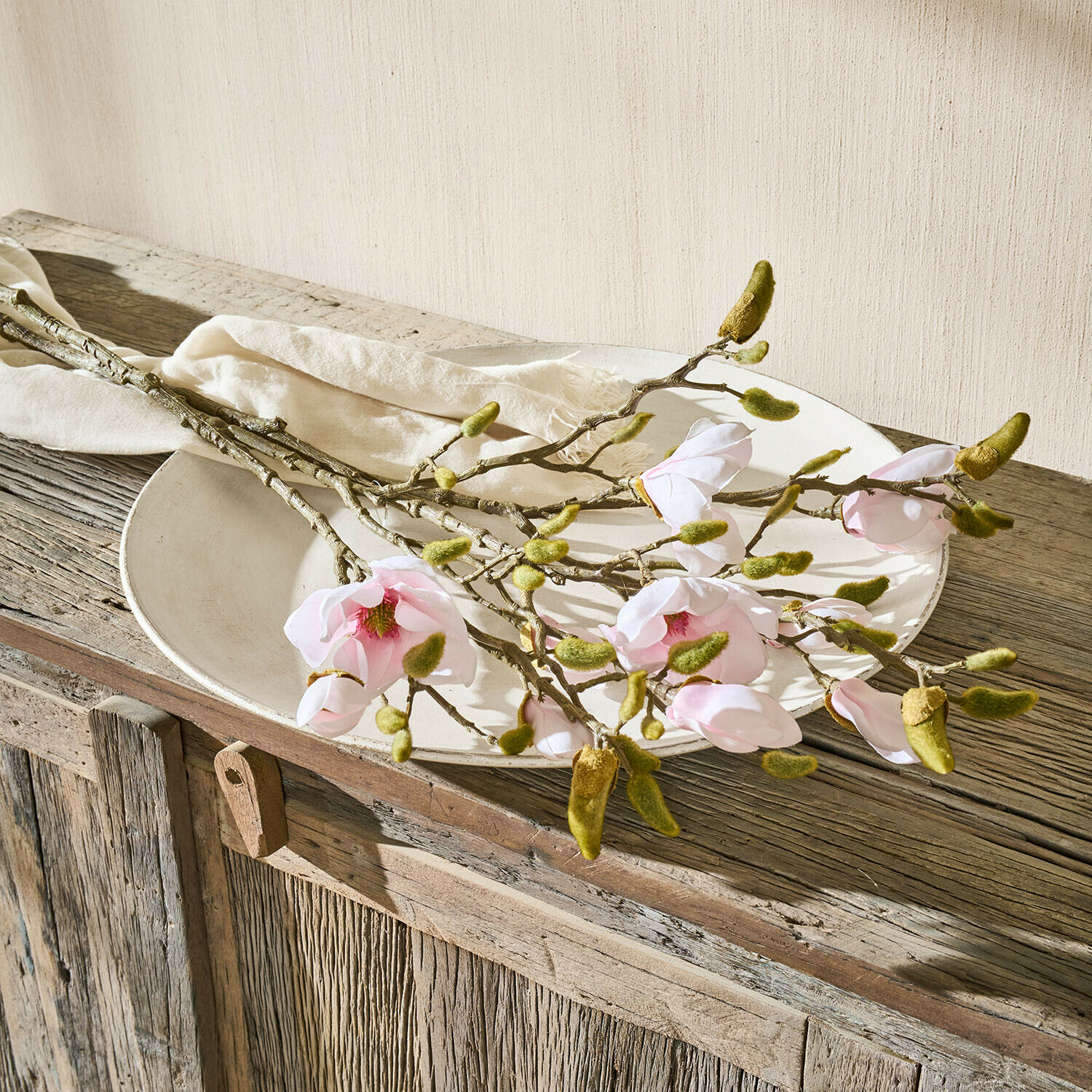 Rami di magnolia con fiori rosa e boccioli verdi su piatto bianco su tavolo in legno rustico