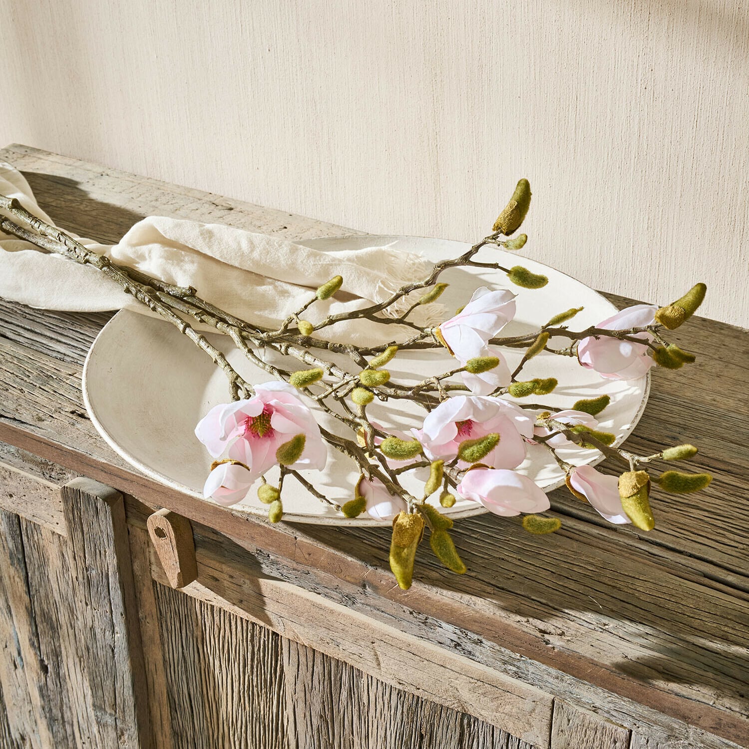 Coppia di fiori decorativi Aurélines Rami di magnolia con fiori rosa e boccioli verdi su piatto bianco su tavolo in legno rustico