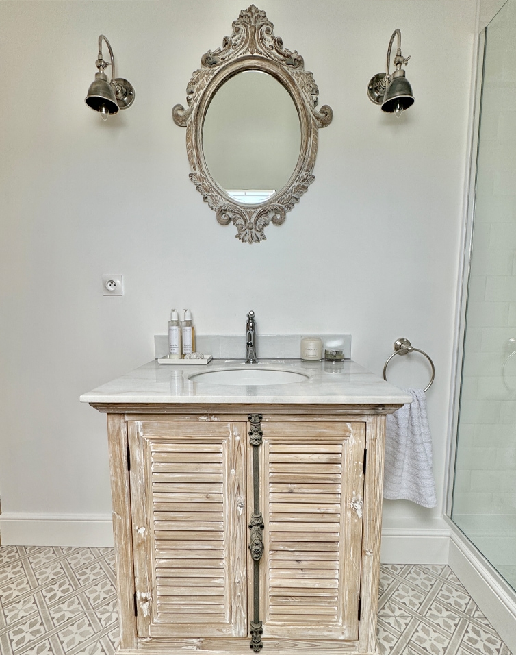 Bagno con mobiletto in legno vintage sotto lavabo e specchio ovale decorativo a parete