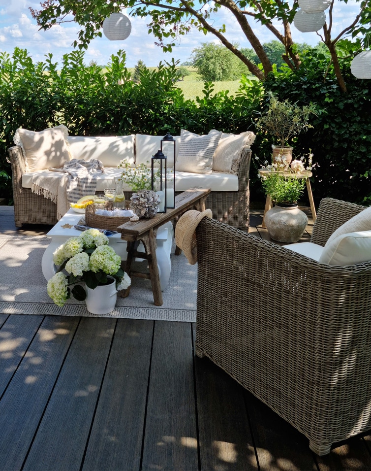 Set di mobili da giardino in rattan con cuscini beige su terrazza decorata con fiori e lanterne