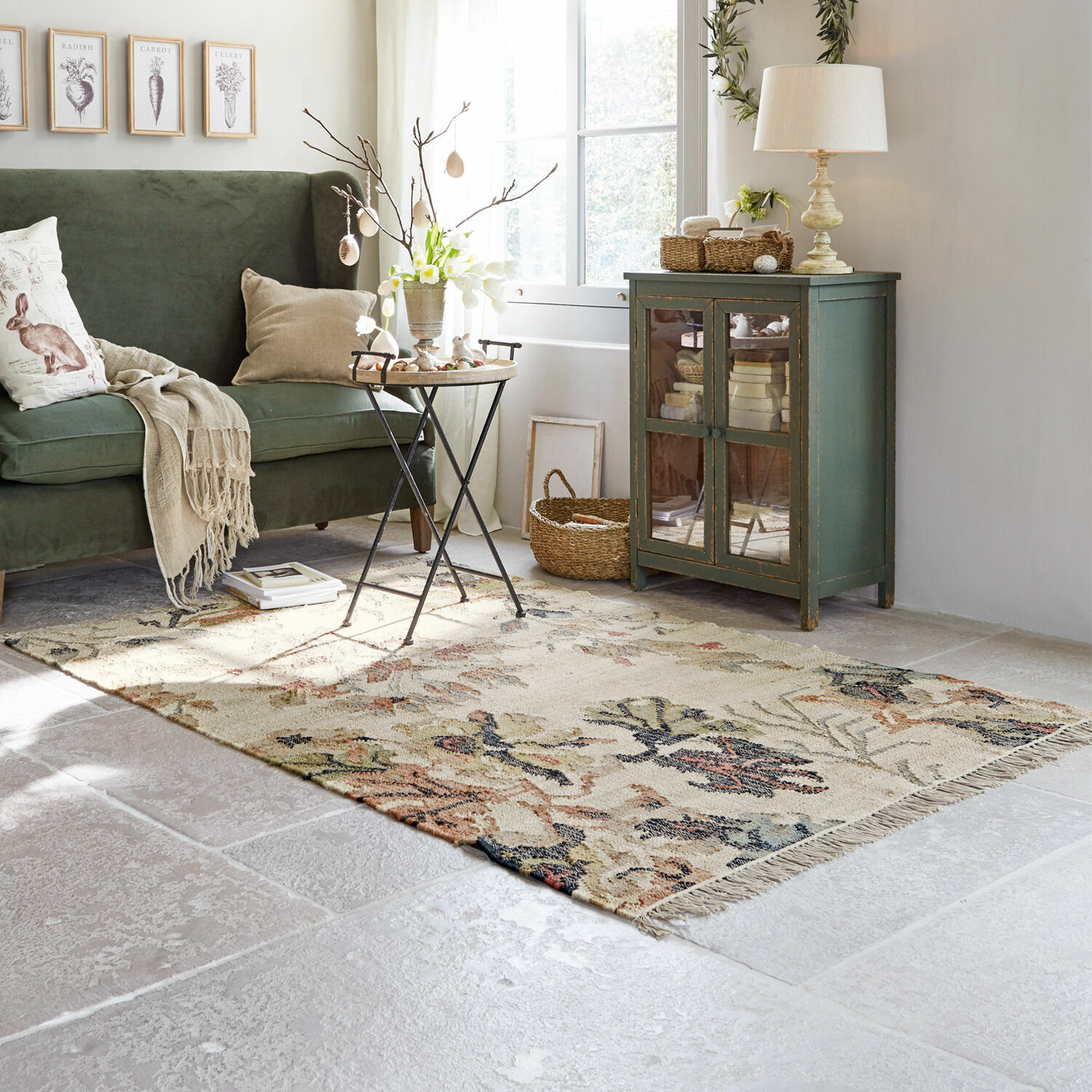 Tappeto Osorno Soggiorno accogliente con divano verde, tappeto beige a motivo floreale e mobile in legno vintage