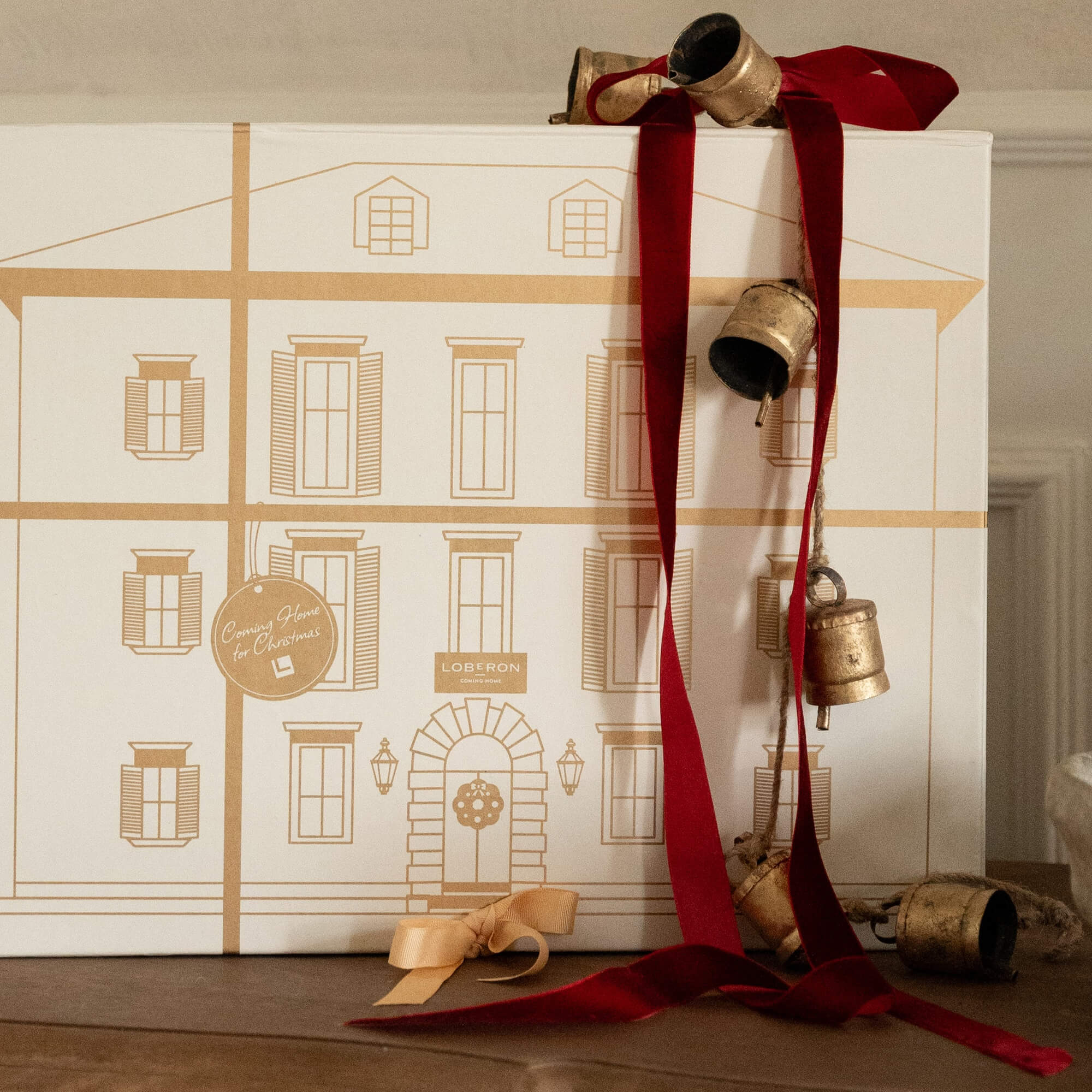 Decorazione natalizia con campanelle metalliche dorate su nastro rosso e scatola decorativa beige
