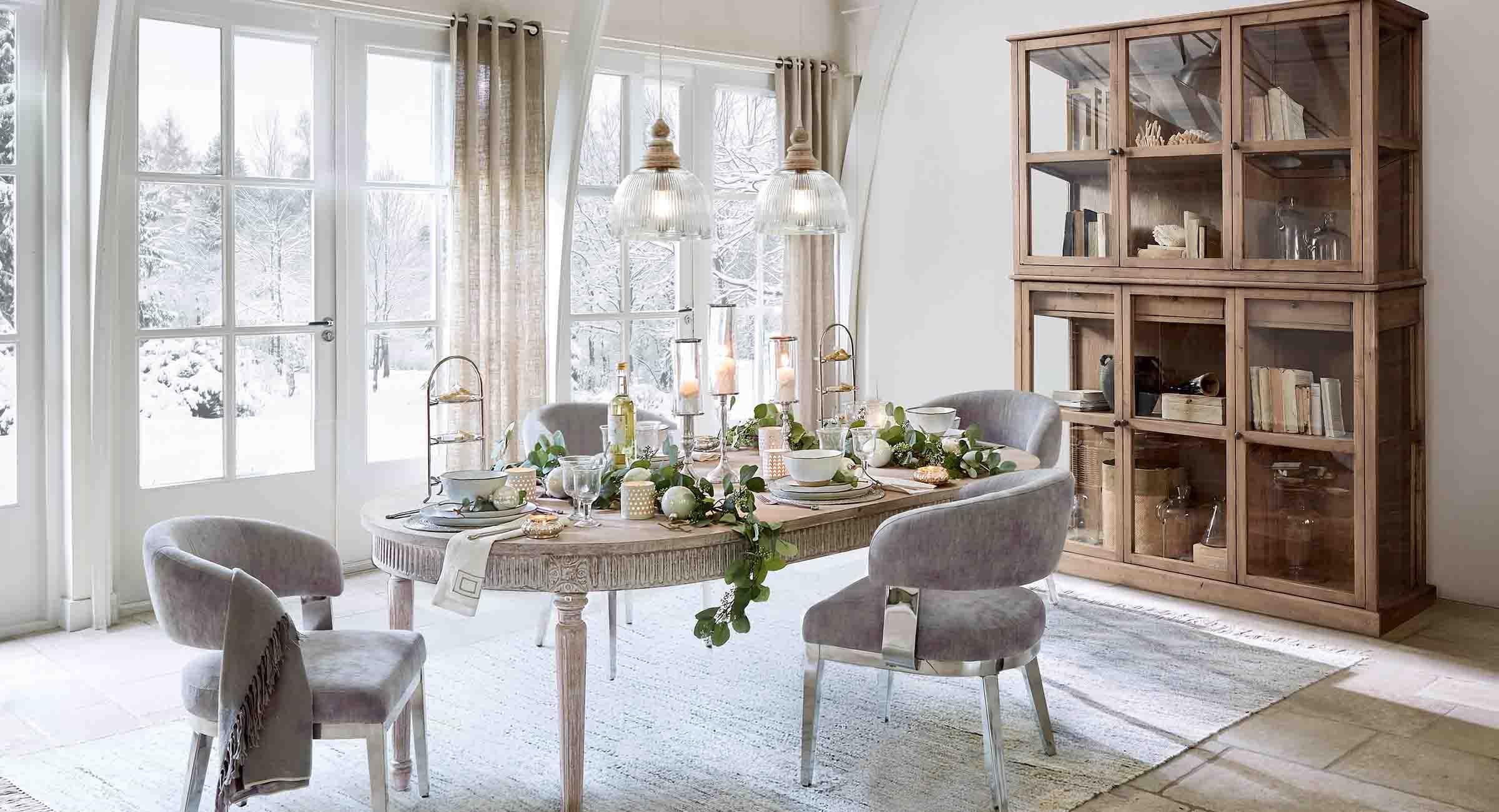 Sala da pranzo con tavolo in legno e sedie grigie decorata per l'inverno con vista su giardino innevato