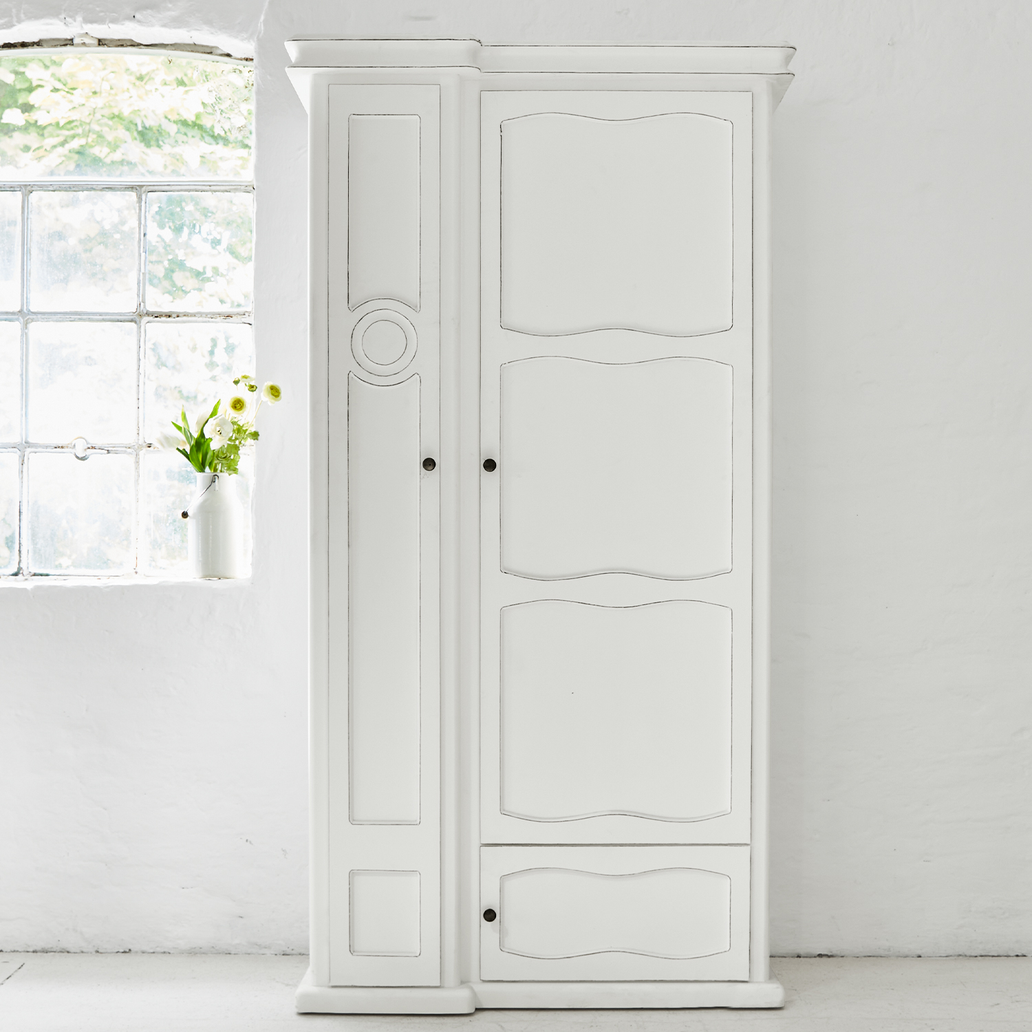 Armadio in legno bianco con pannelli decorativi e maniglie in metallo in ambiente luminoso