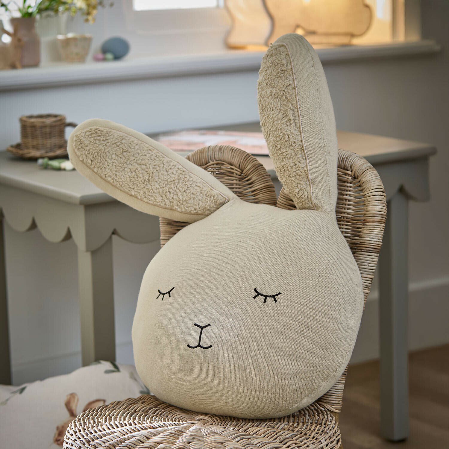 Cuscino Fuzzletop Cuscino beige a forma di coniglio in tessuto morbido su sedia in vimini in camera dei bambini