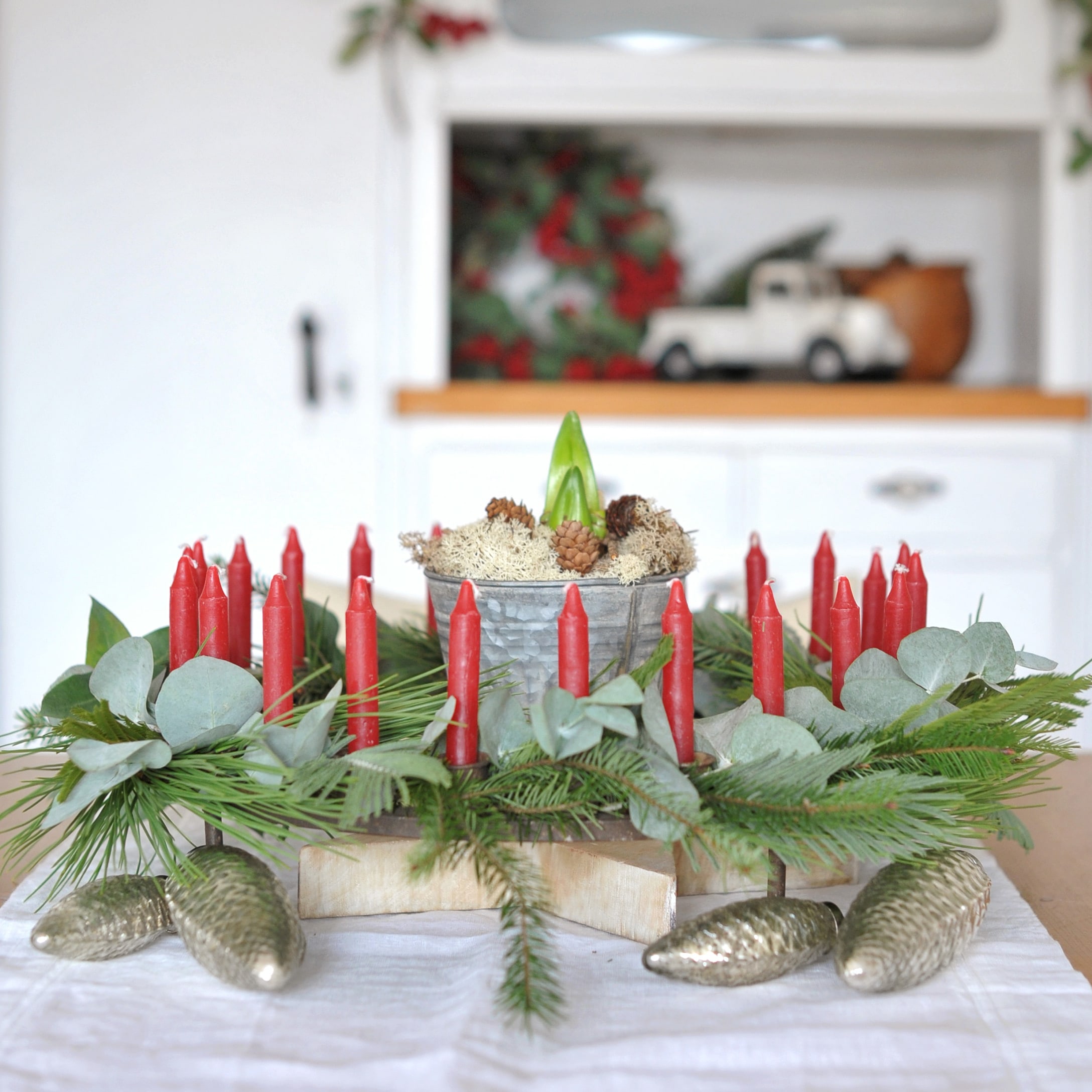 Corona d'Avvento decorativa con candele rosse, rami verdi e pigne metalliche sul tavolo