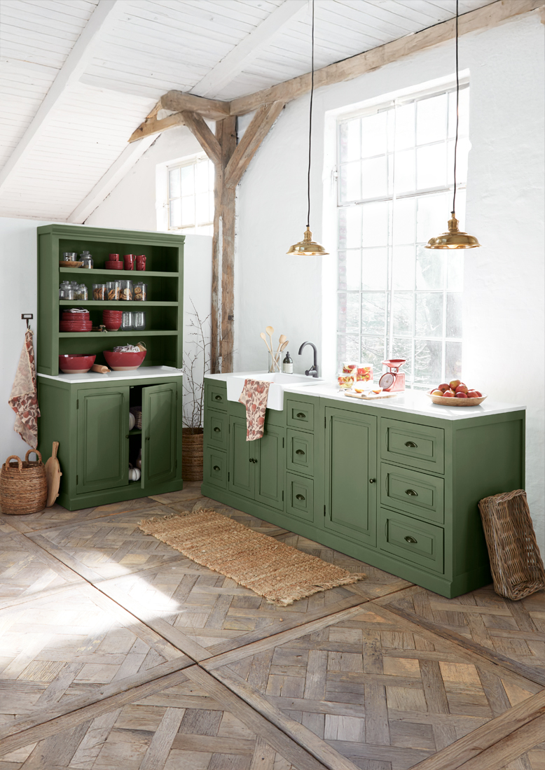 Cucina in legno verde con piano bianco e lampade in ottone in interno rustico luminoso