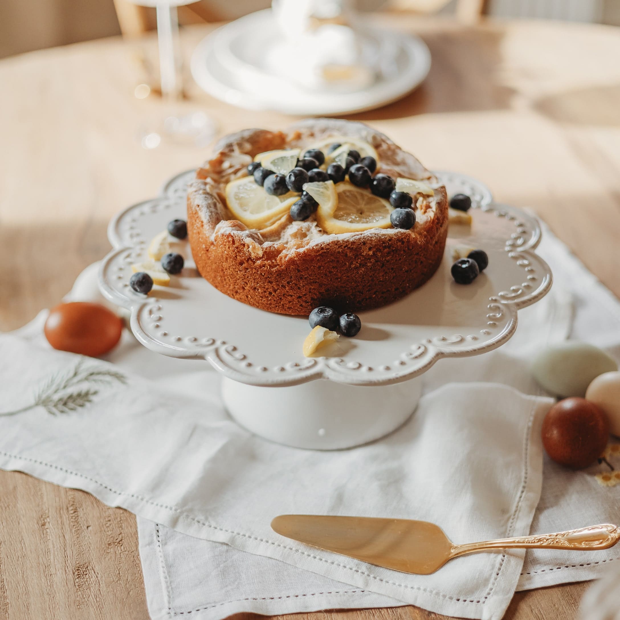 Torta con fette di limone e mirtilli su alzata in ceramica bianca su tavolo di legno
