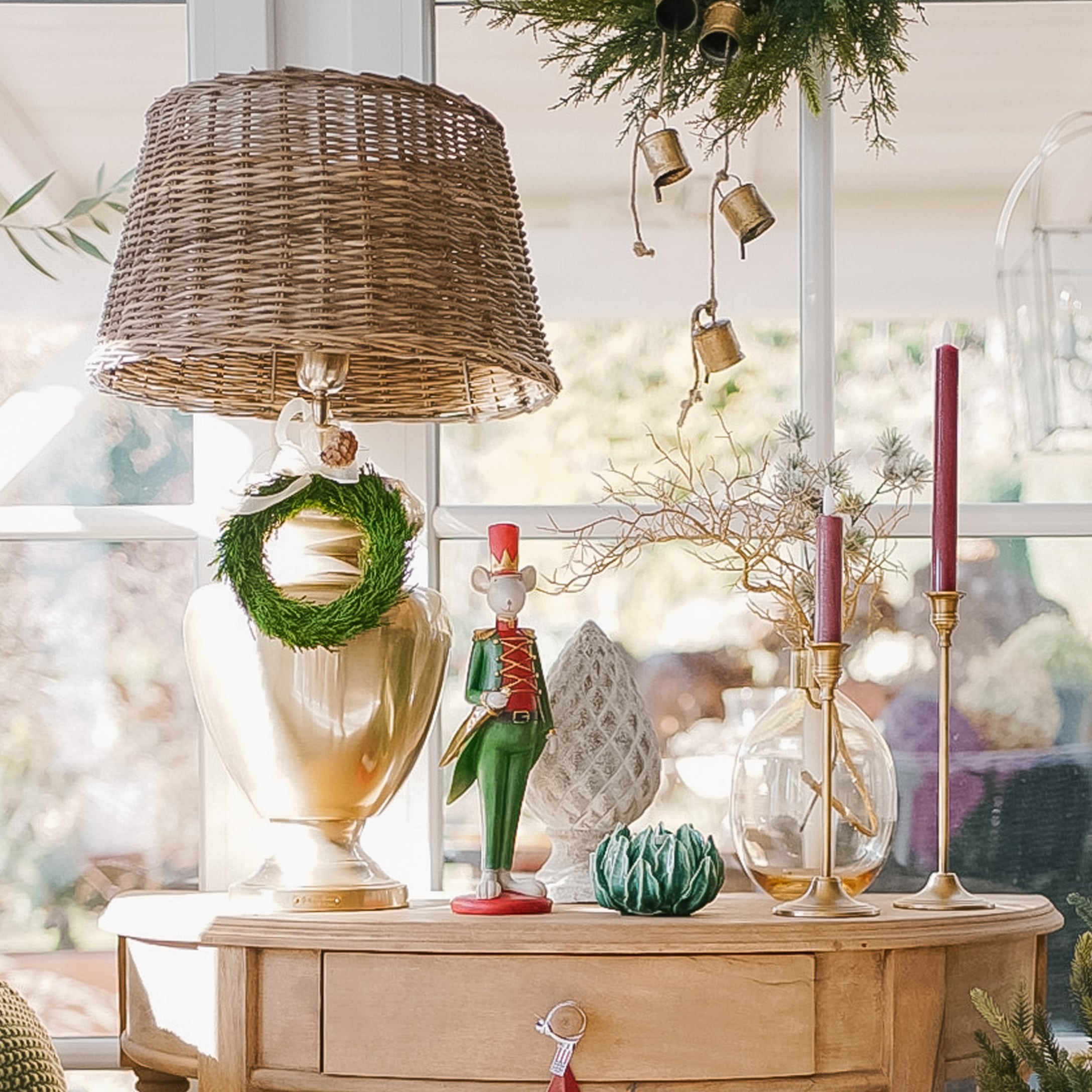 Lampada decorativa con paralume in vimini e decorazioni natalizie su tavolo in legno chiaro