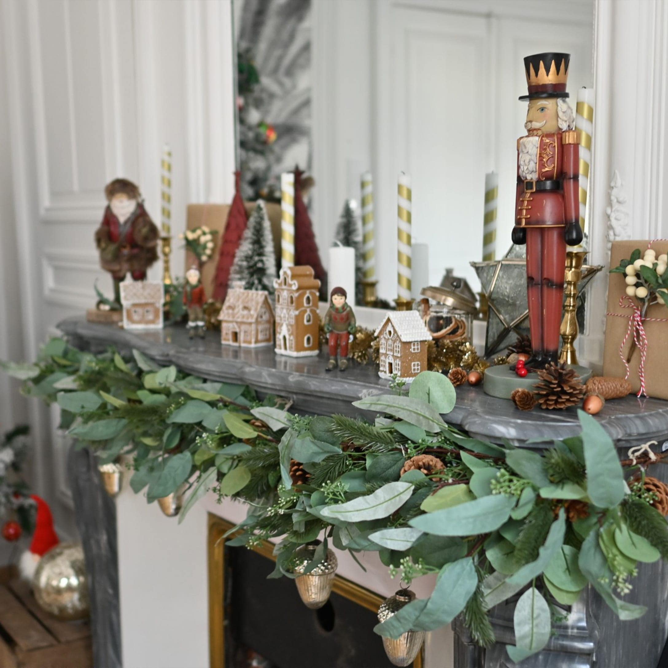 Decorazione natalizia su camino con rami verdi, pigne e figura di schiaccianoci su marmo grigio