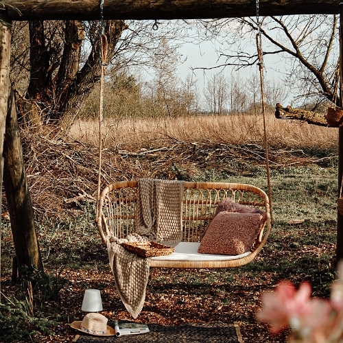 Altalena in rattan naturale con cuscino e coperta in giardino autunnale