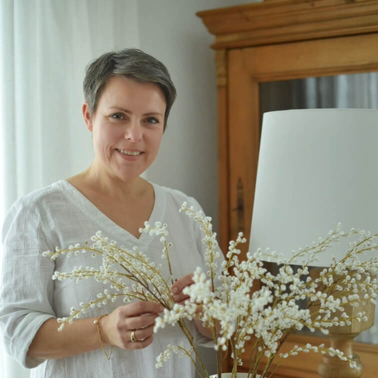 Donna con camicia bianca che tiene rami decorativi con fiori bianchi in interno luminoso