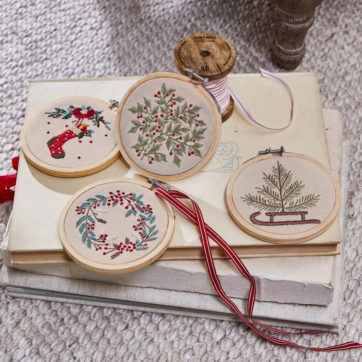 Set di quattro decorazioni natalizie ricamate con motivi vegetali e dettagli rossi su sfondo beige