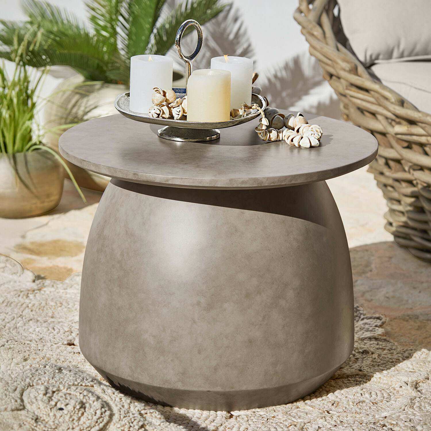 Tavolino rotondo in cemento grigio con candele e decorazioni di conchiglie su terrazza