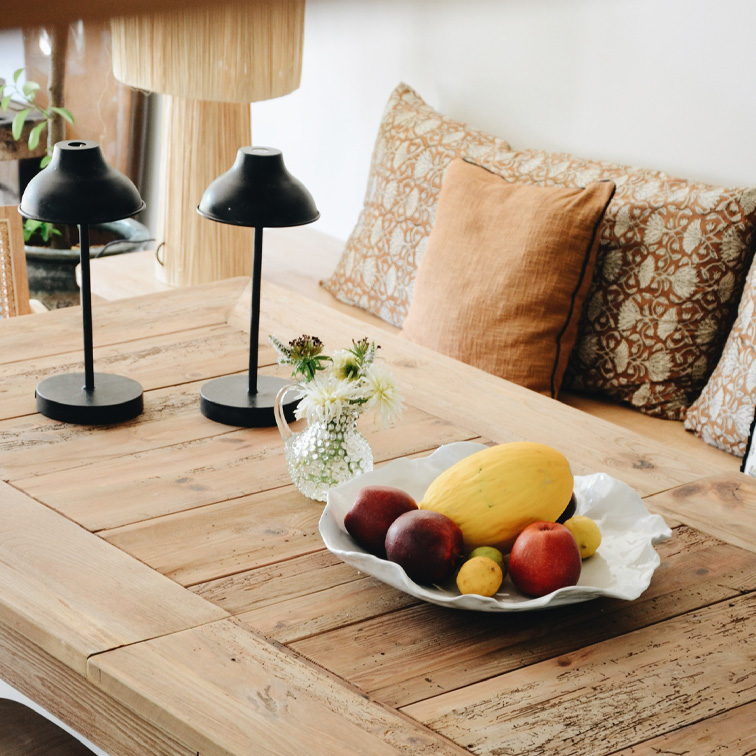 Tavolo in legno con ciotola bianca decorativa con frutta e due lampade nere in un ambiente accogliente
