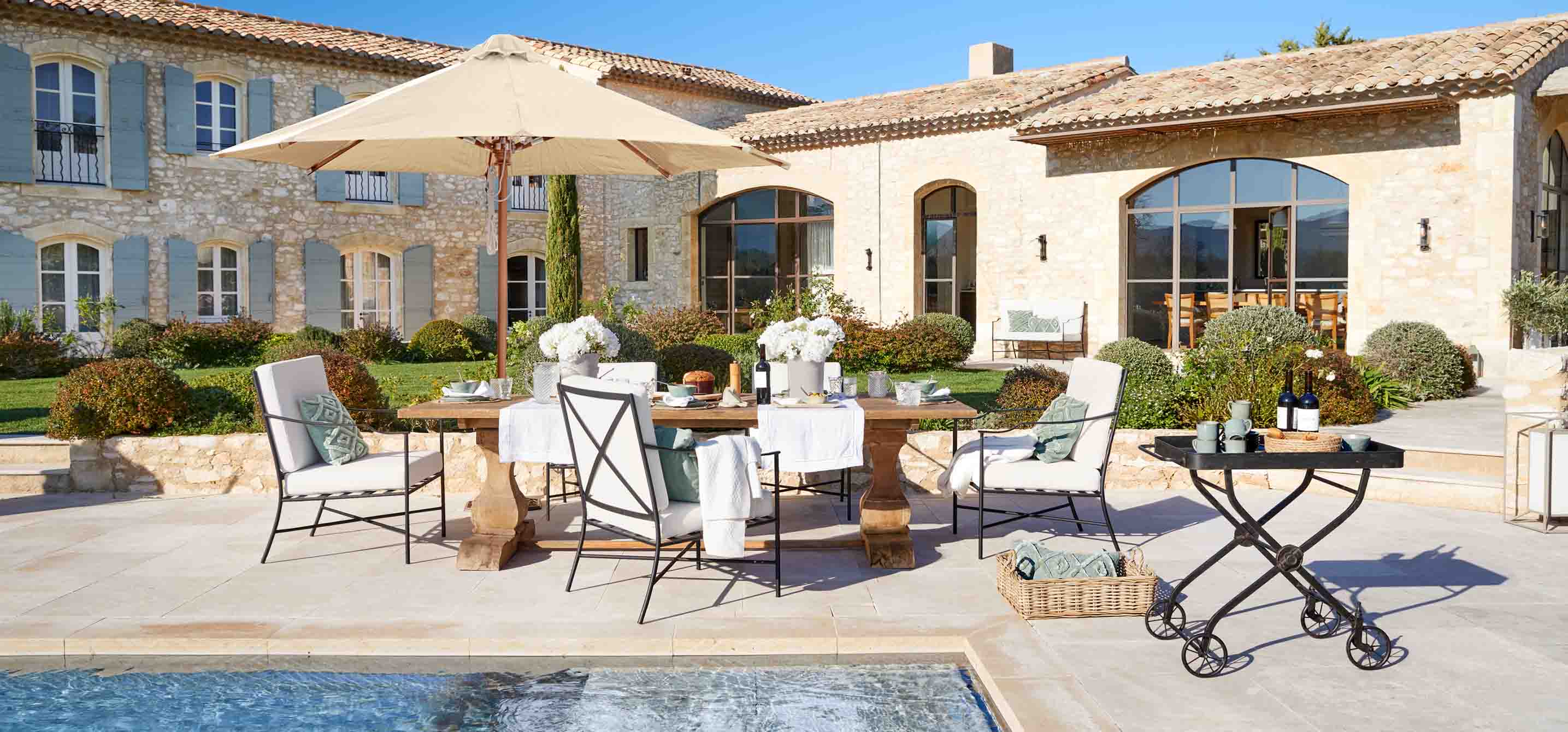 Set di mobili da giardino con tavolo in legno e cuscini crema vicino alla piscina in stile rustico